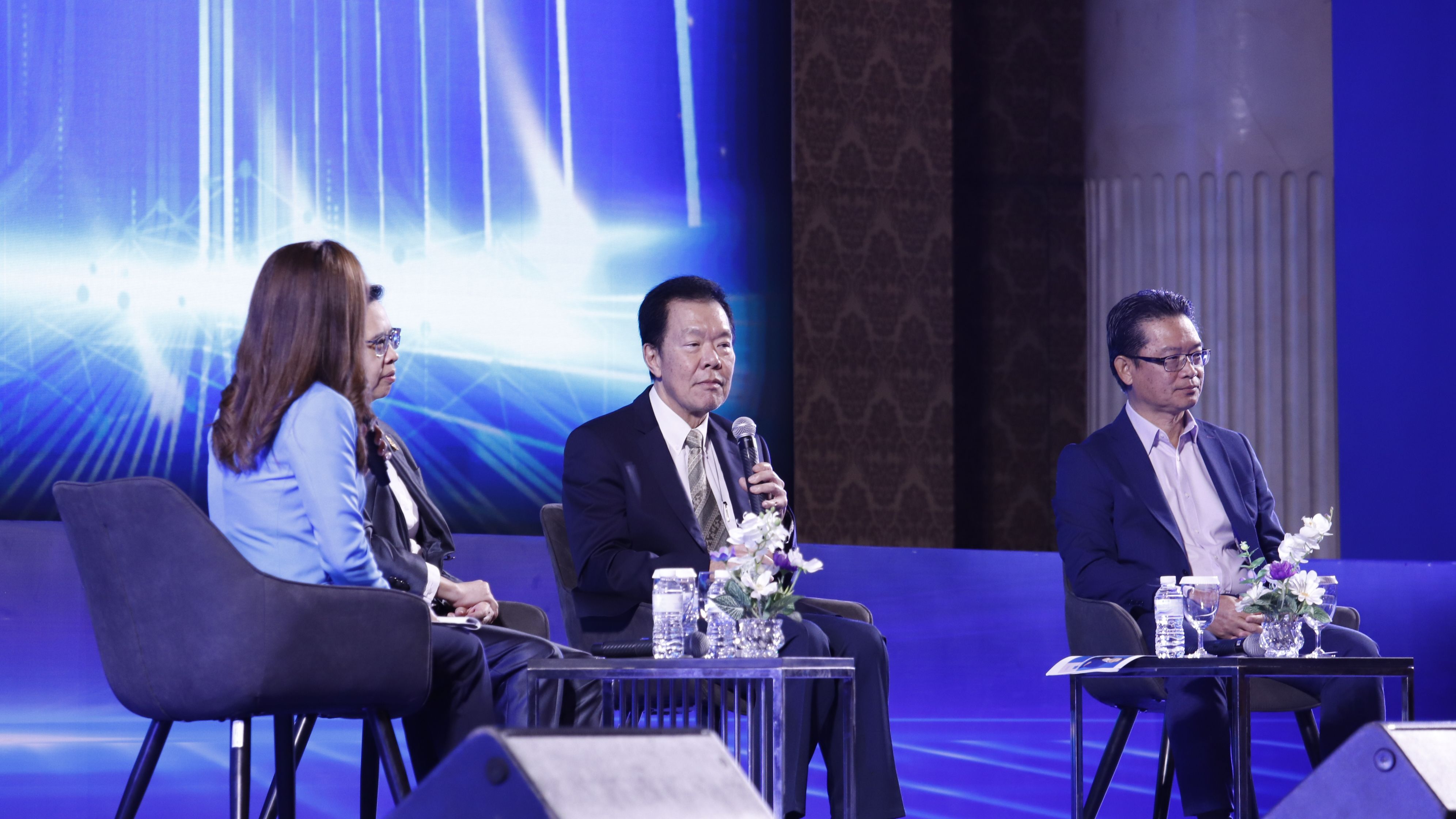 Man speaking into a microphone at a panel discussion with three other participants on stage.