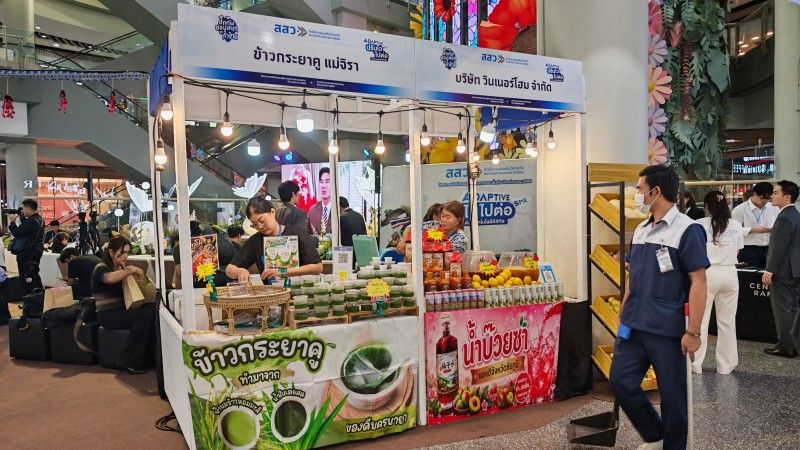 Two market stalls showcase beverages and natural products at a lively indoor event.