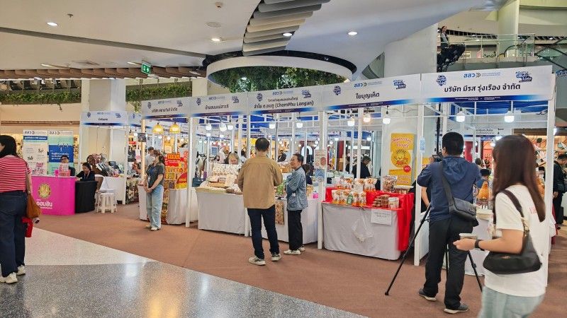 People browse diverse products at white-canopied market stalls inside a brightly lit exhibition hall.