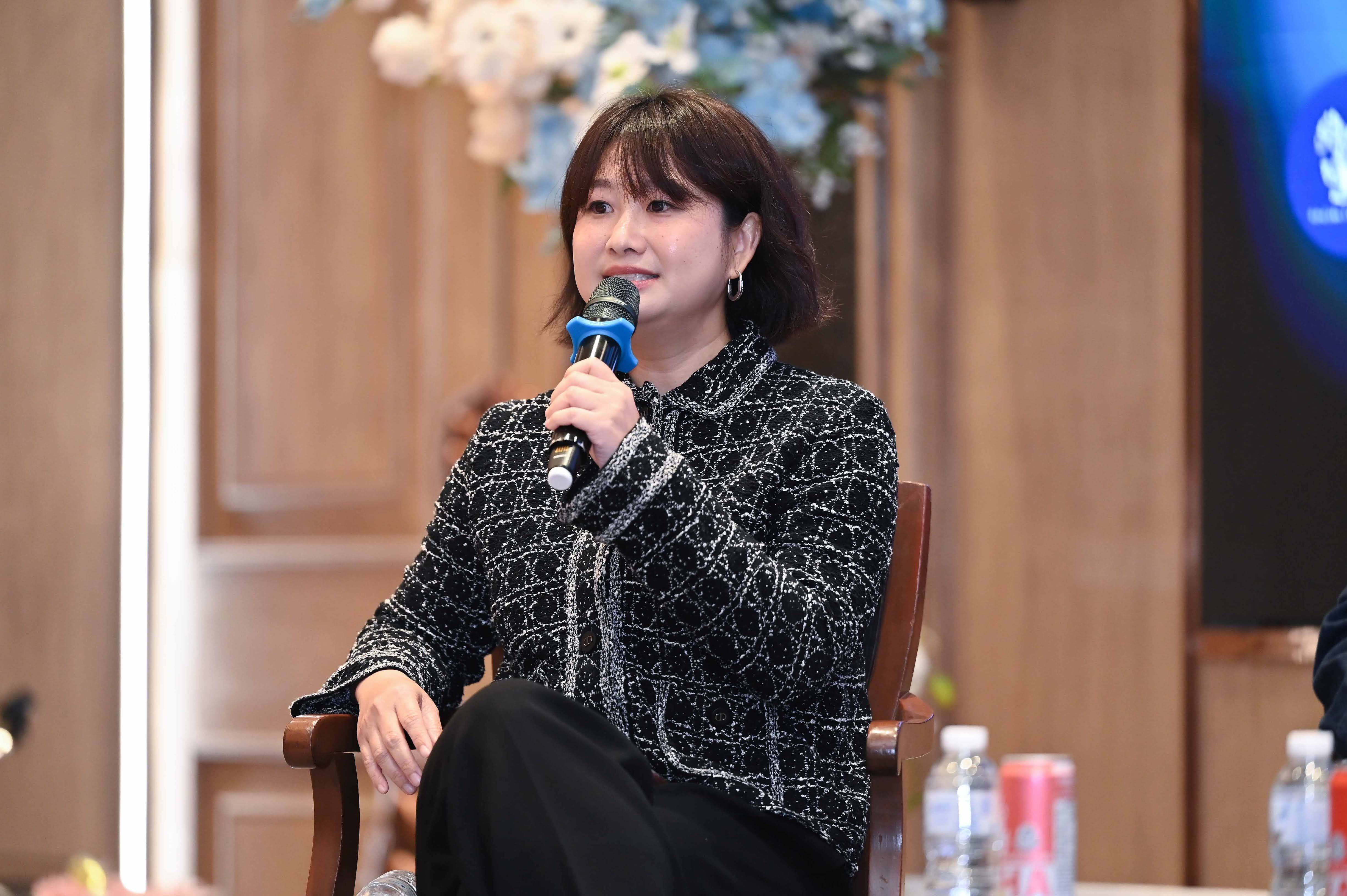 A woman with short dark hair speaks into a microphone at an event.