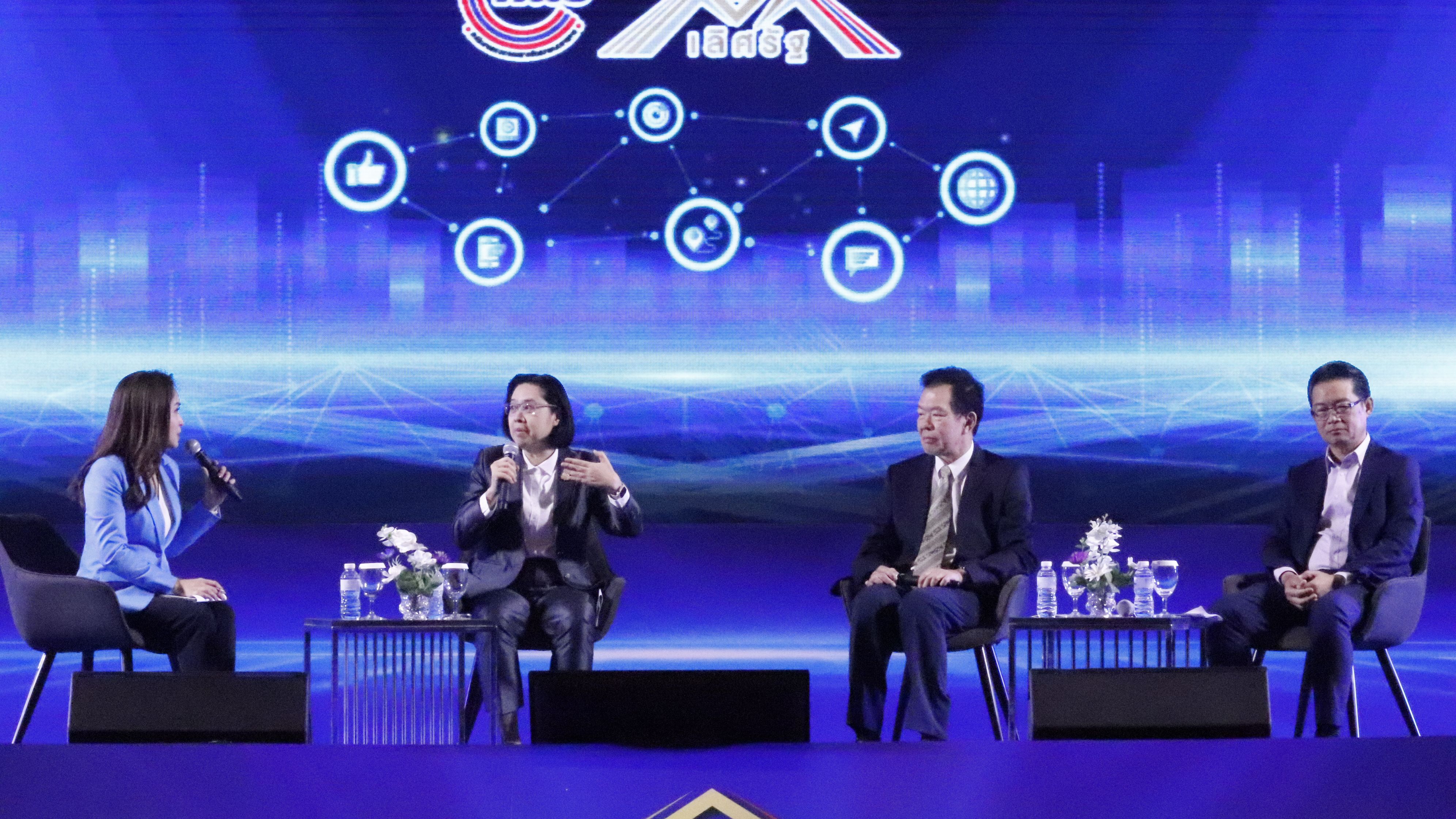 Four panelists on stage discussing, with a digital background screen showing interconnected icons.