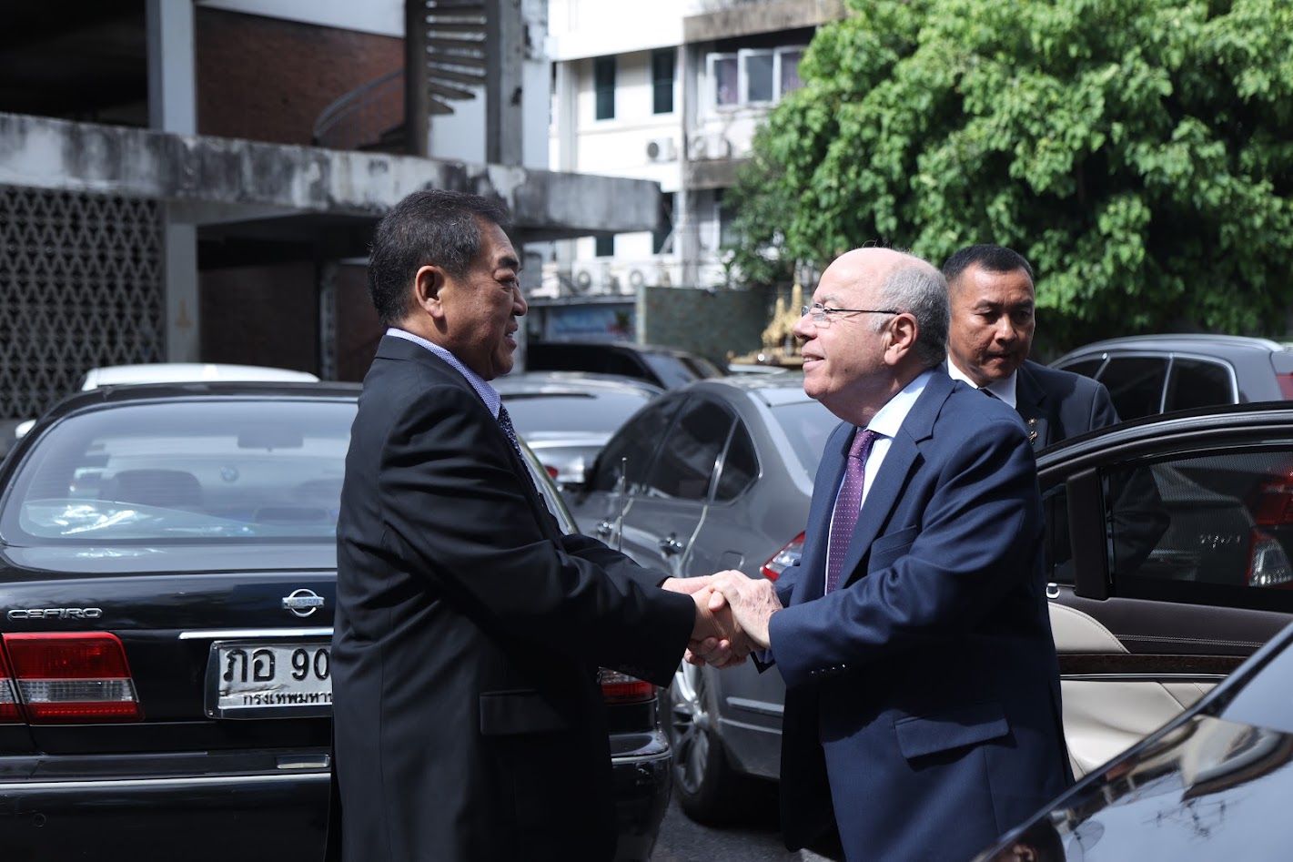 Two distinguished men in suits shaking hands warmly outdoors, signifying a formal meeting.