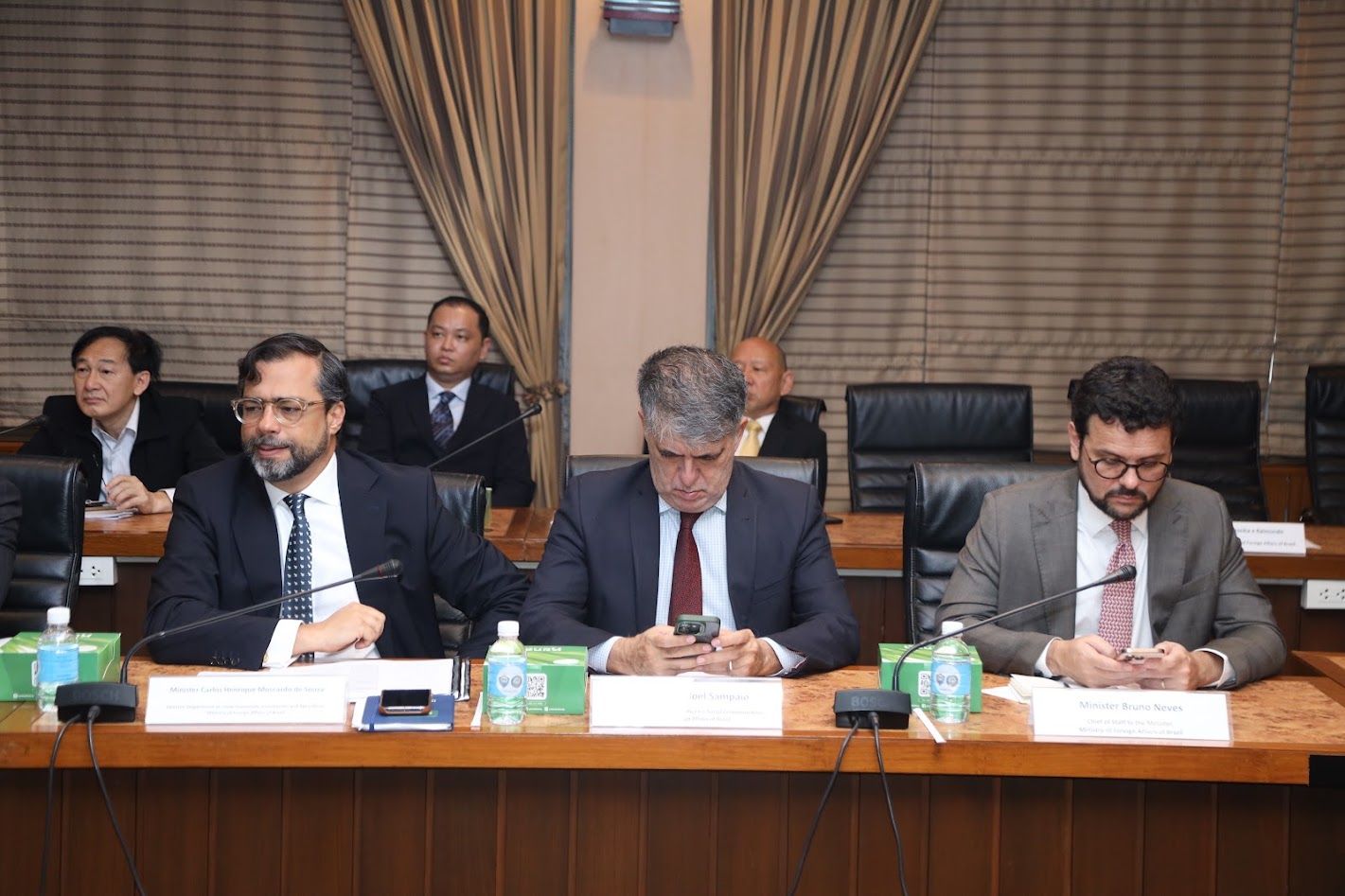 Three men in suits seated at a conference table during a formal meeting.