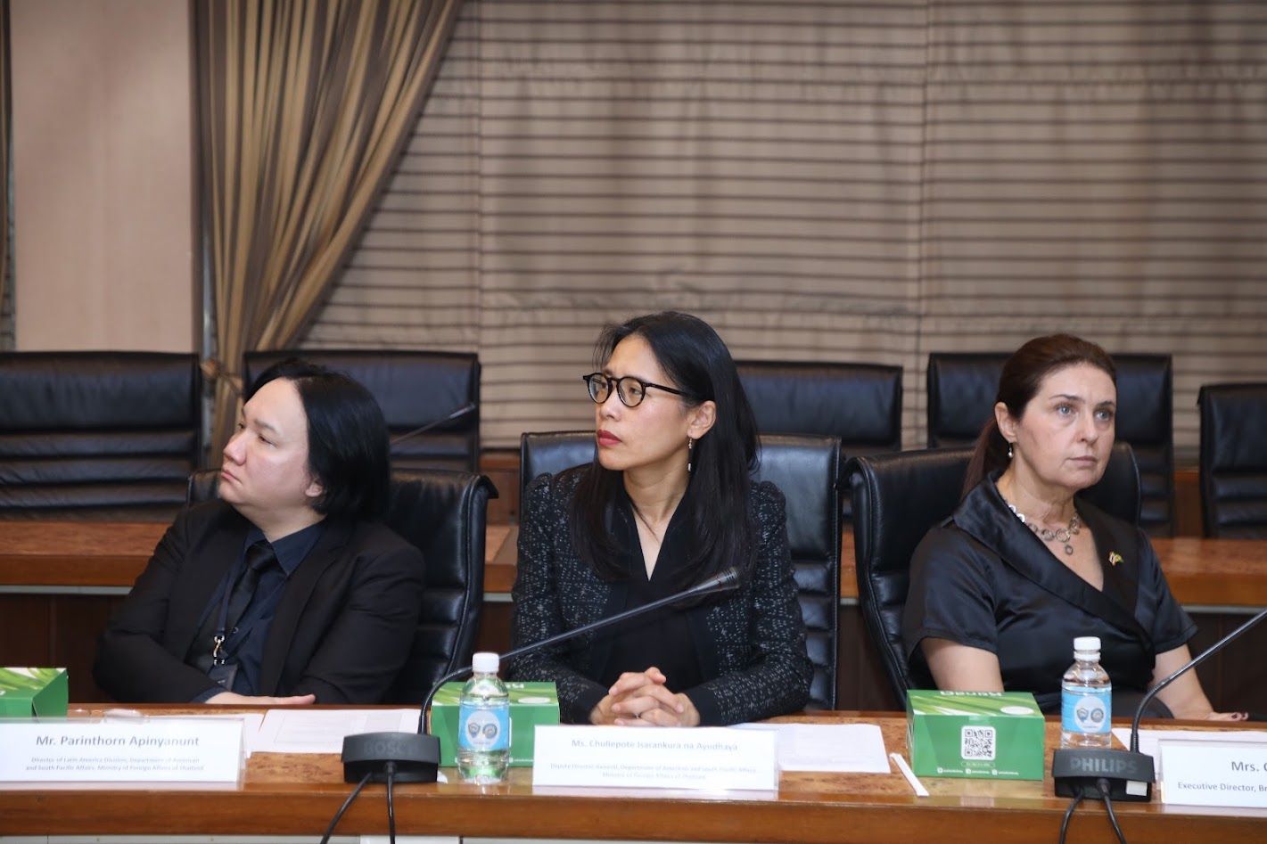 Three professional women sit at a conference table, attentively looking left.