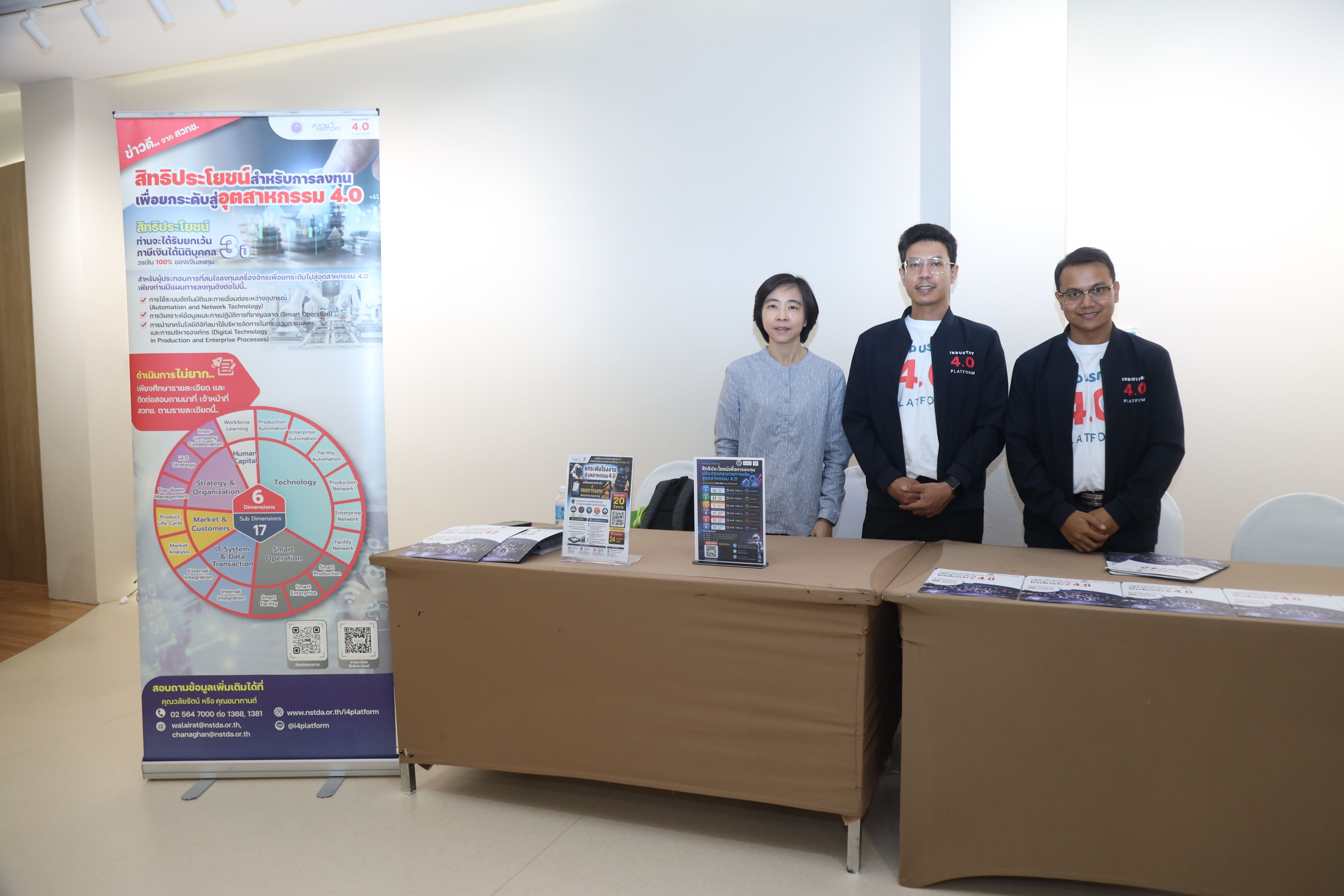 Three people stand behind tables at an informational booth with a banner display.