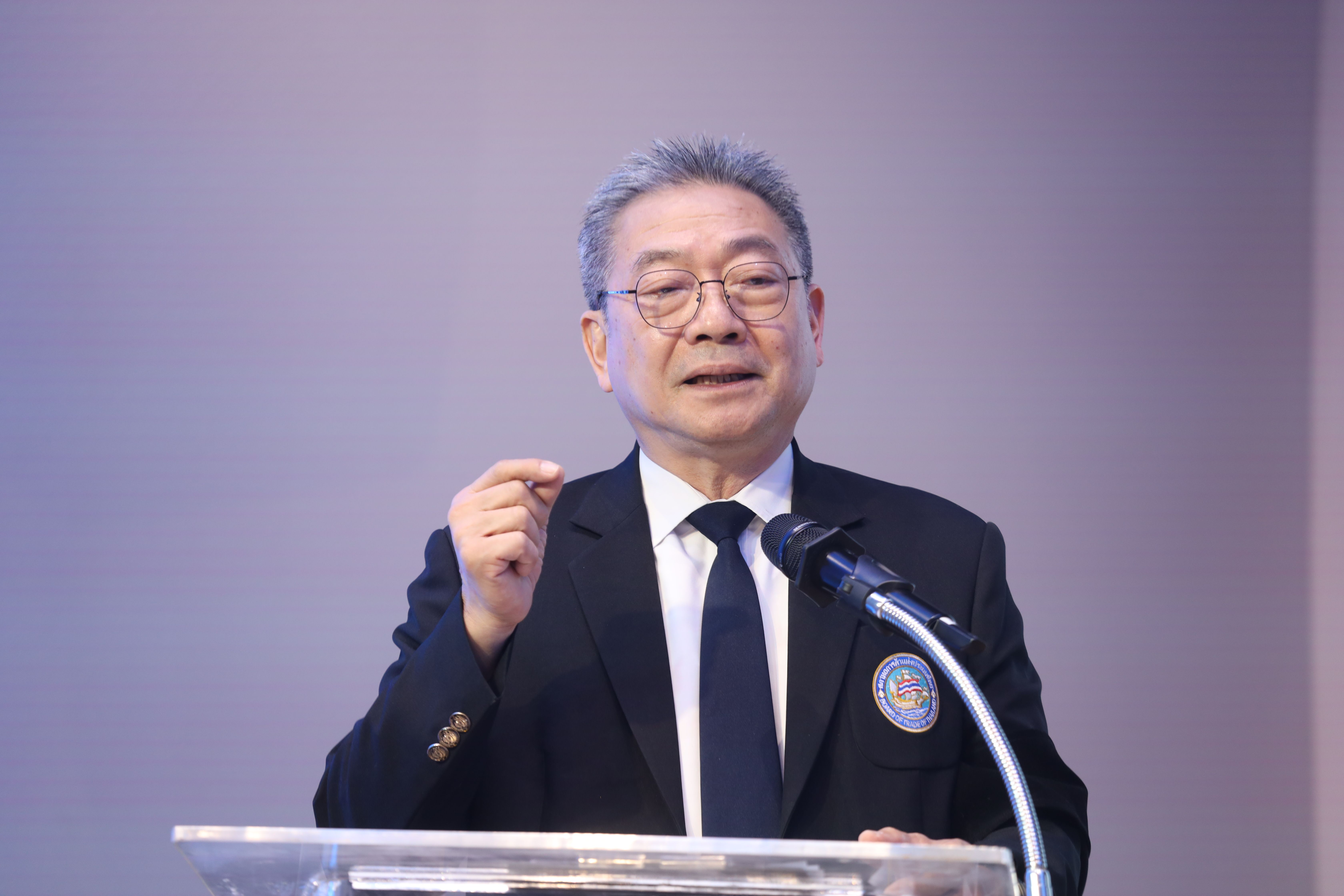 Older Asian man in a suit speaks at a podium, gesturing thoughtfully.