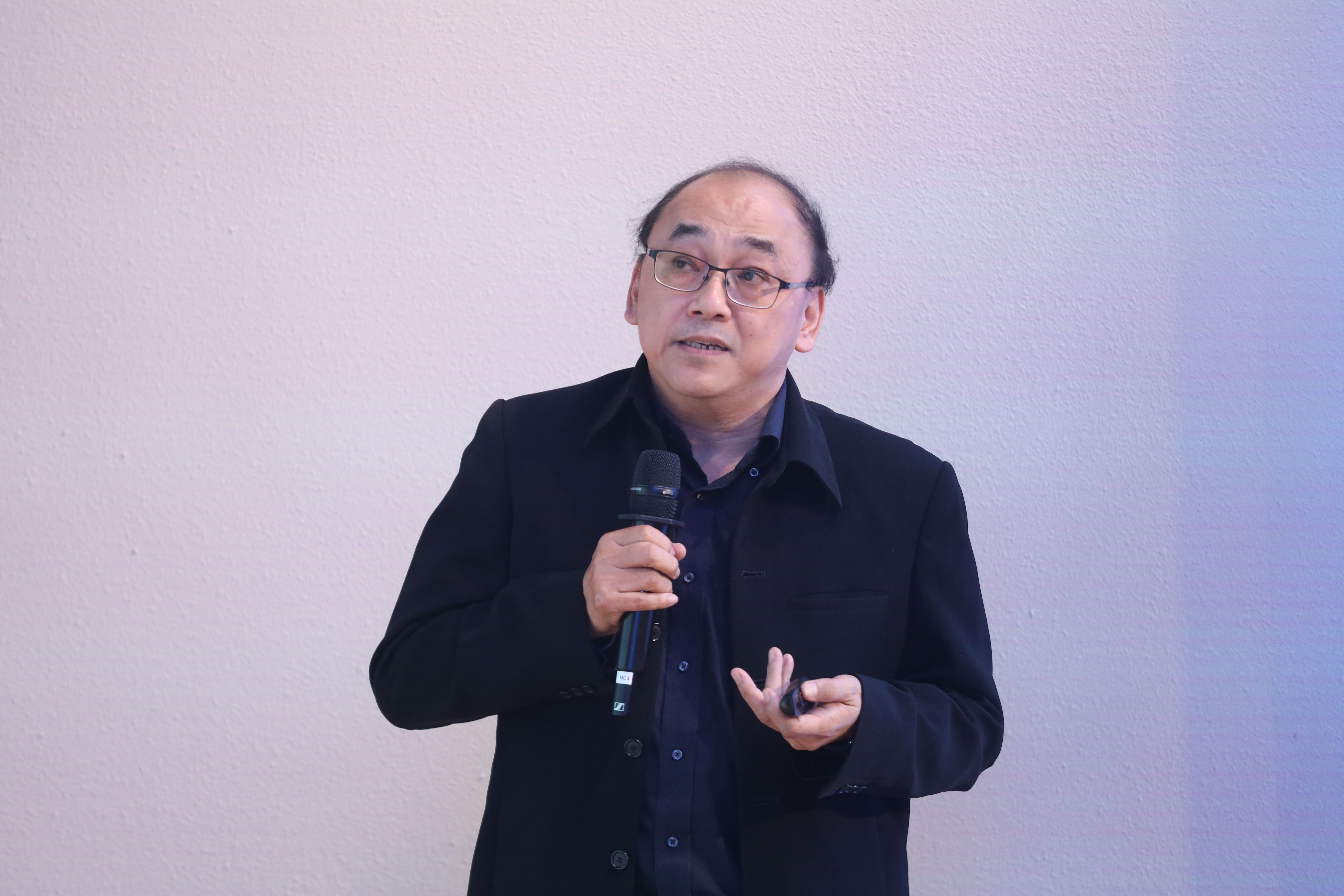 Man with glasses speaking into a microphone during a presentation.
