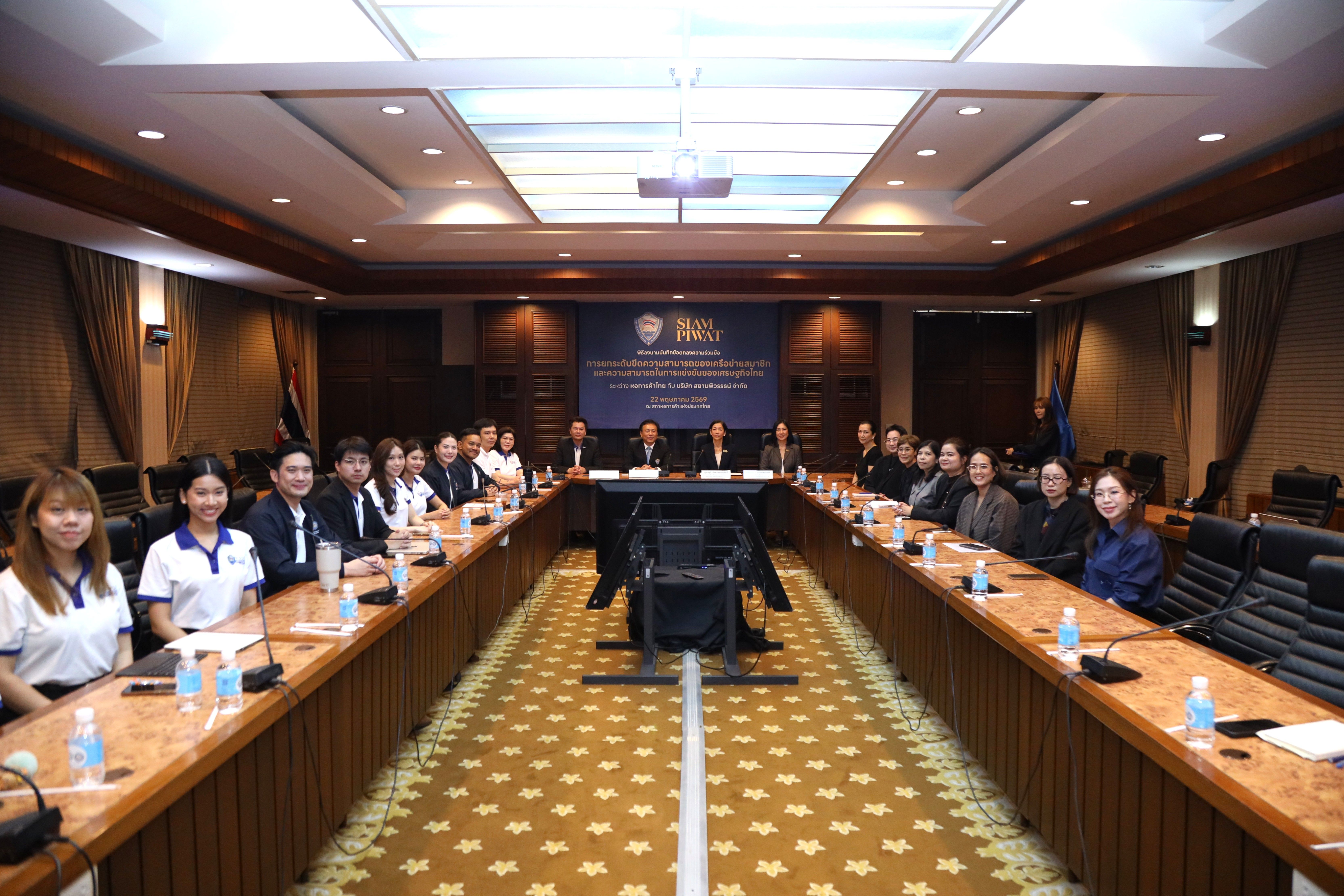Attendees seated at a U-shaped table in a formal conference room with a large screen.