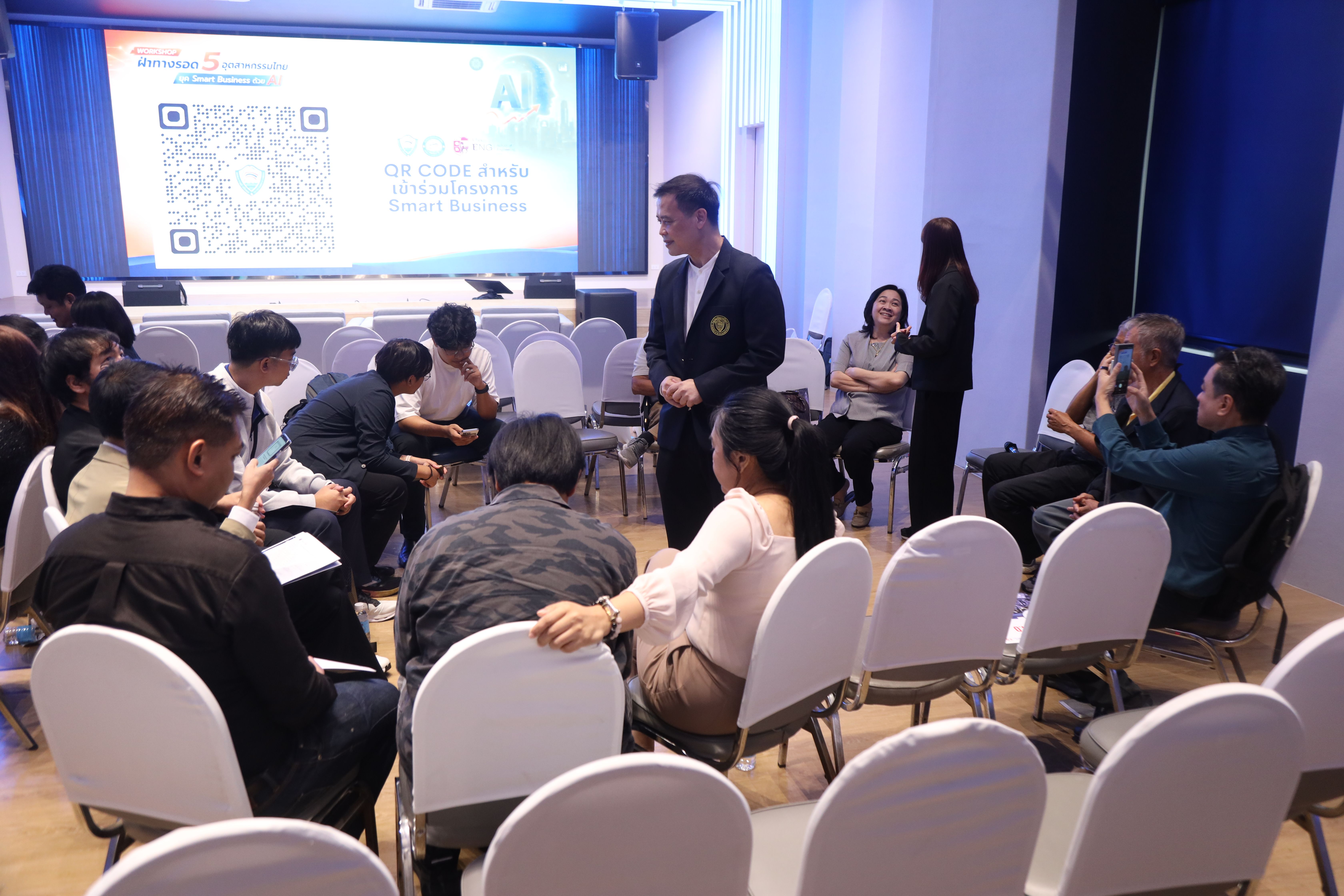 Workshop participants interact while a speaker stands near a large presentation screen.