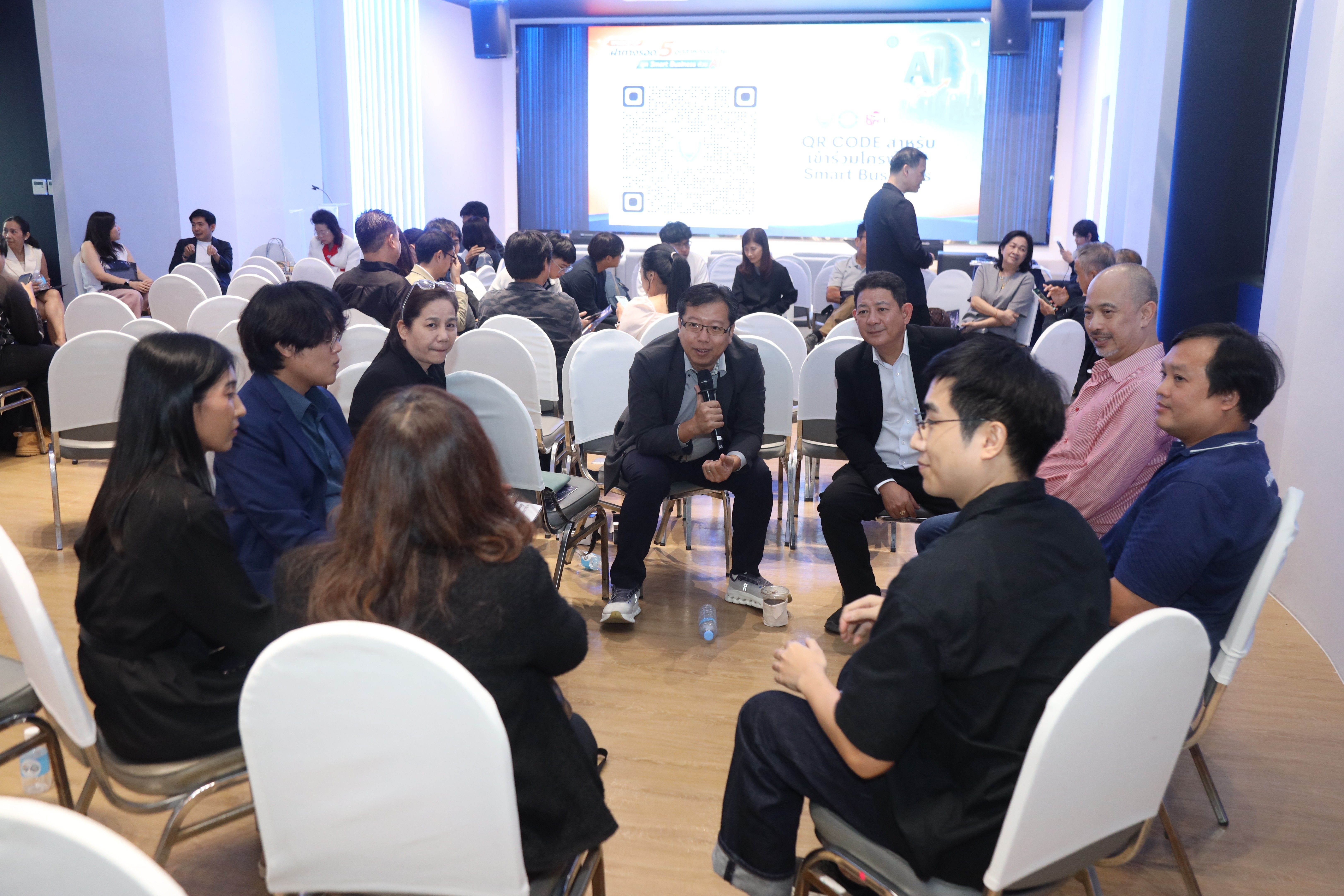 A group of people sitting in a circle, engaged in a discussion led by a speaker with a microphone.