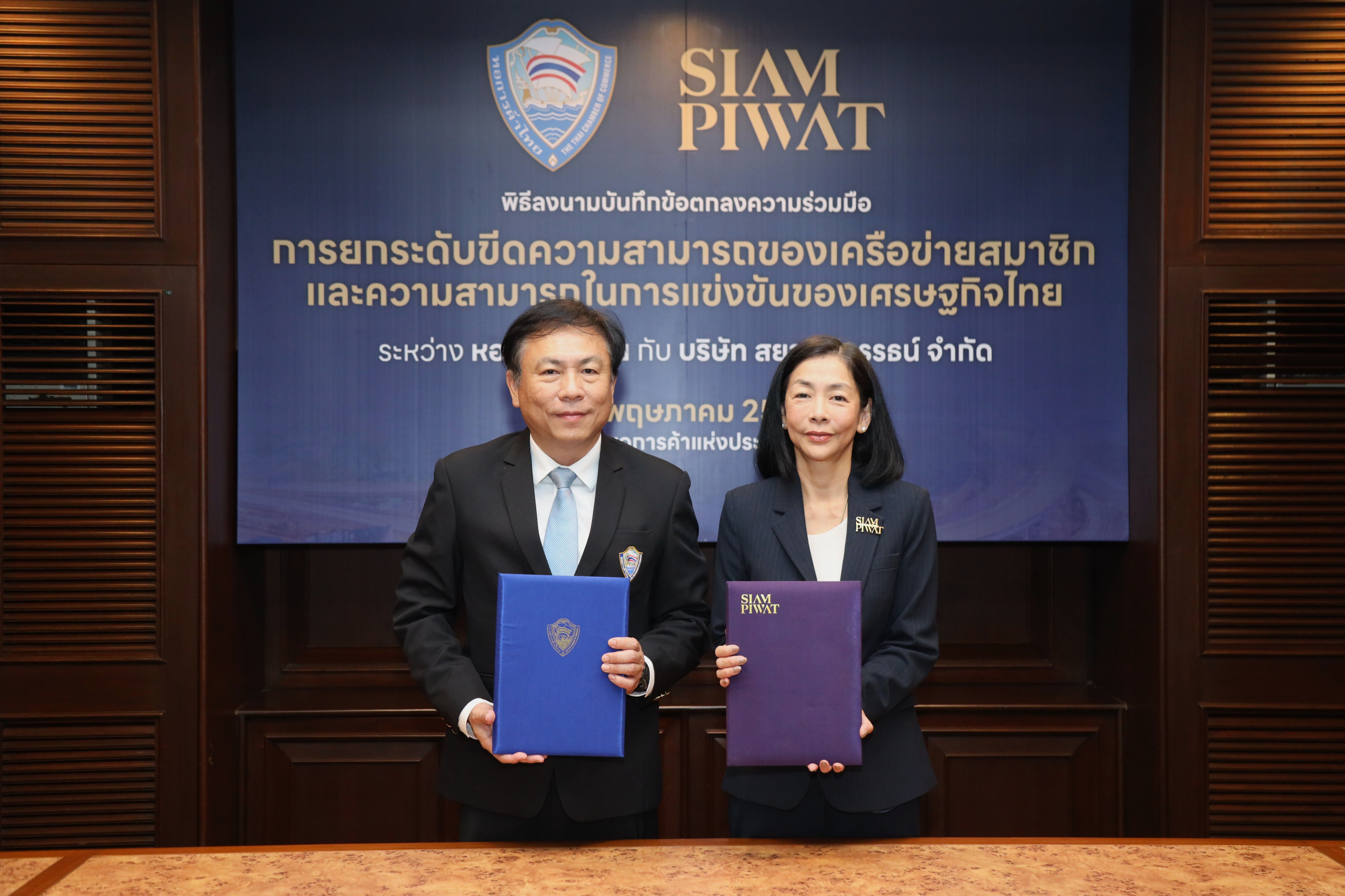 Two executives hold folders in front of a SIAM PIWAT banner after a signing ceremony.