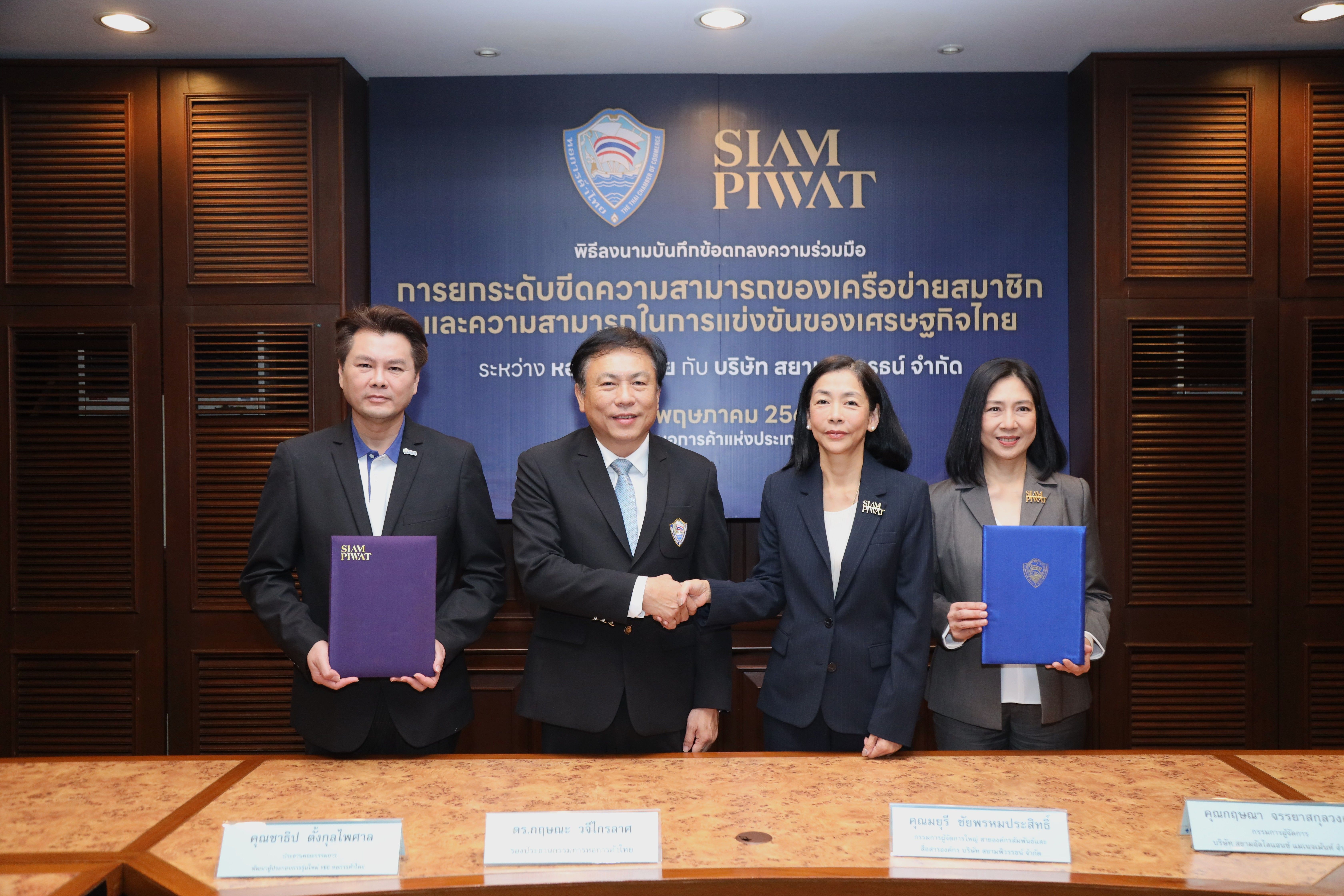 Four people shaking hands in front of a Siam Piwat banner during a formal event.