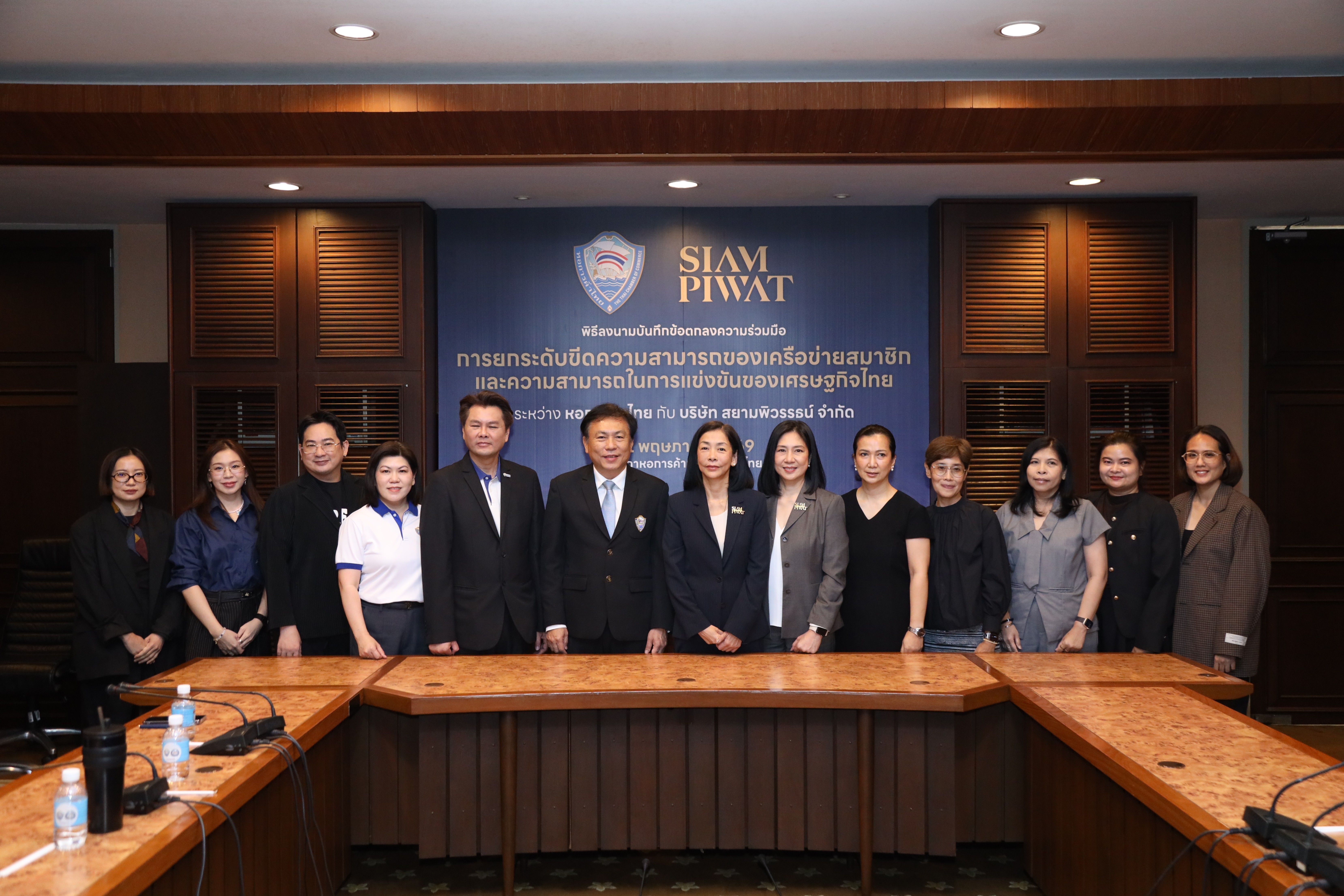 A group of professionals pose in a meeting room before a Siam Piwat banner.