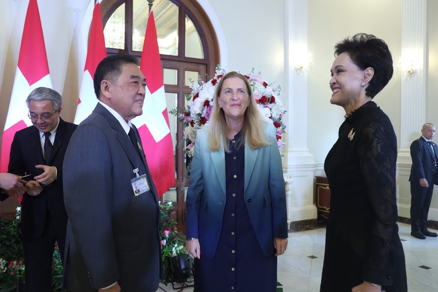 Three diplomats, two women and one man, smiling at a formal diplomatic event.