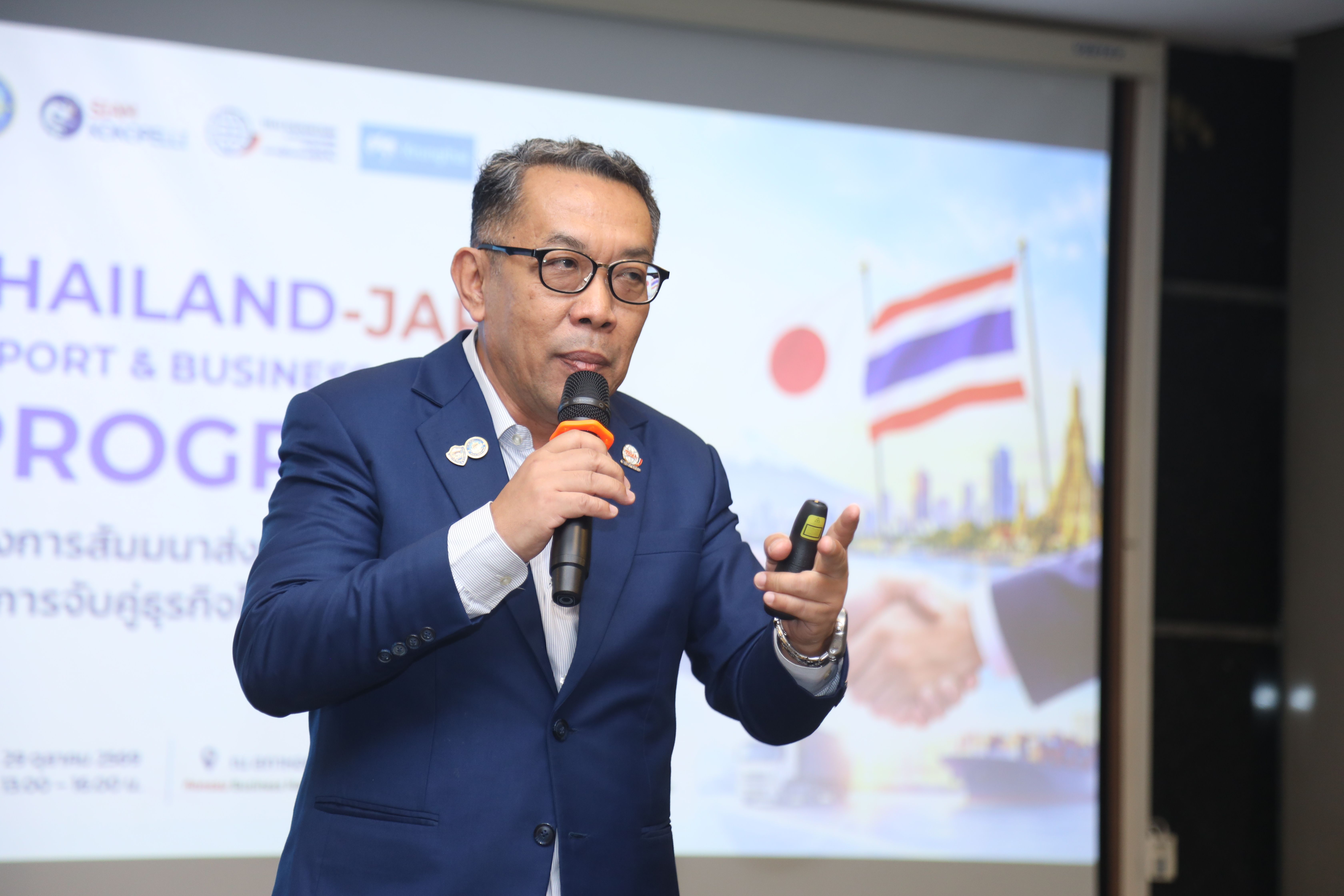 Businessman speaks into a microphone at a presentation about Thailand-Japan trade and business program.