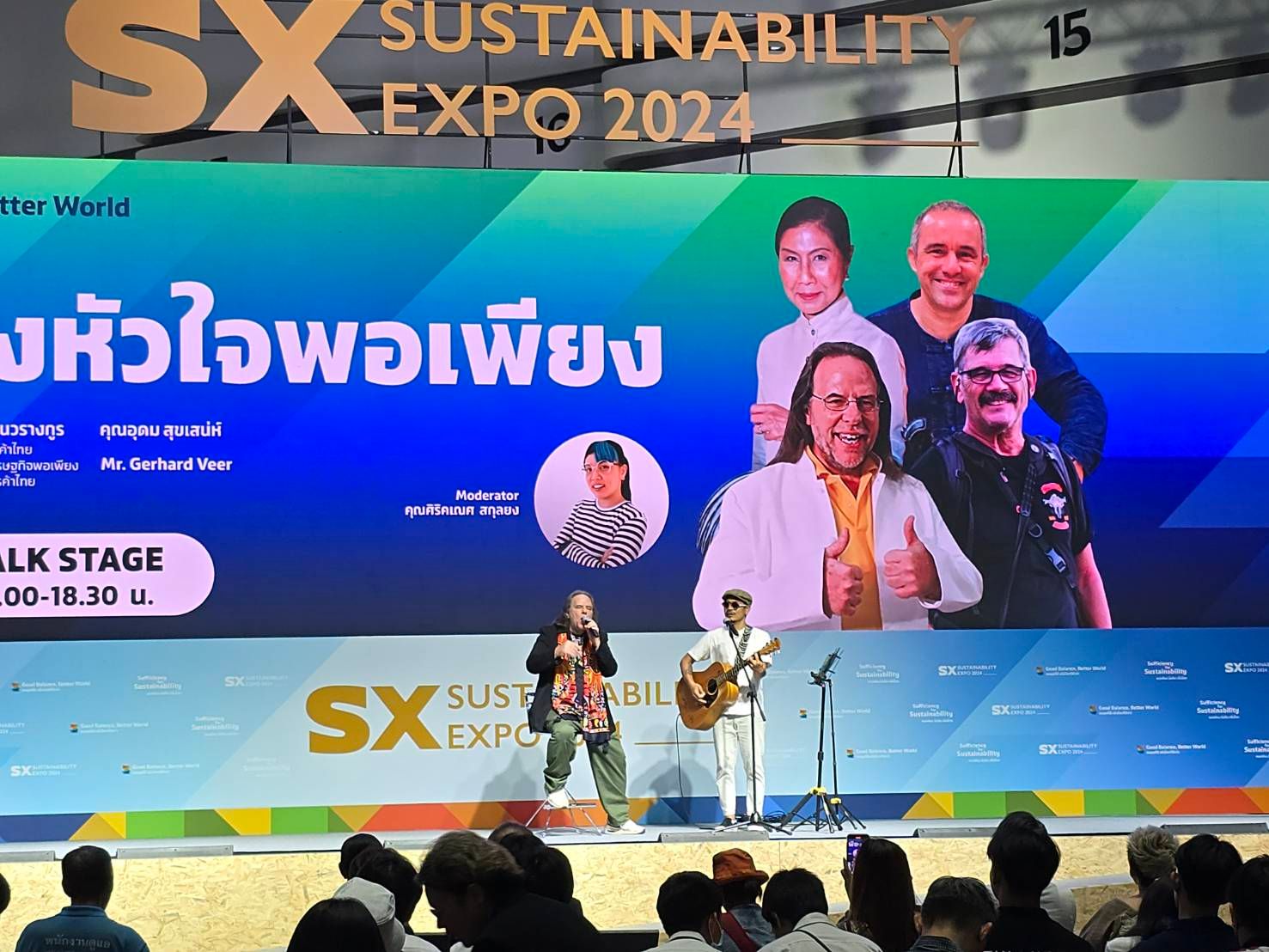 Performers on stage at the SX Sustainability Expo 2024 with a large screen displaying speakers.