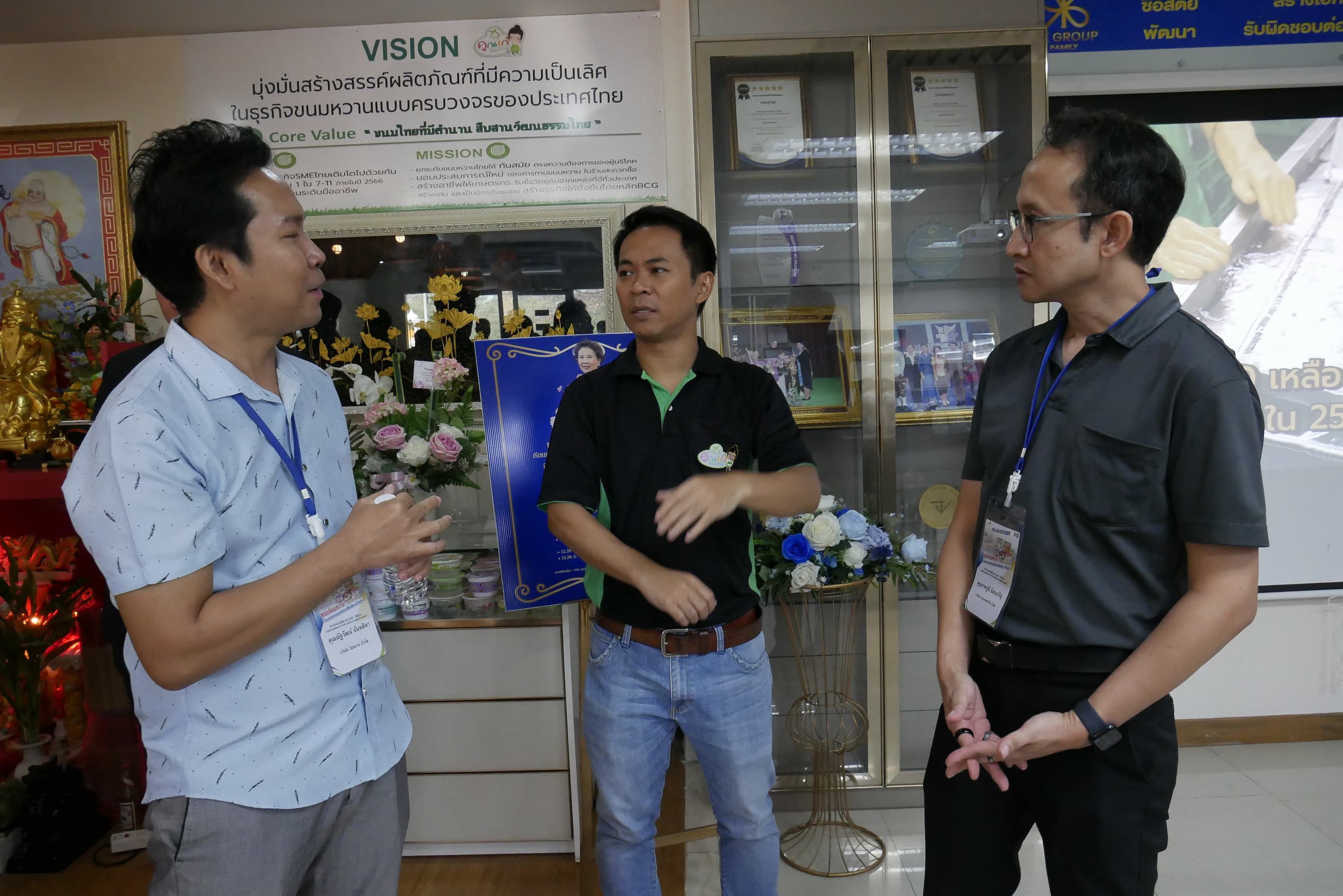 Three men are engaged in a discussion while standing indoors in a professional setting.