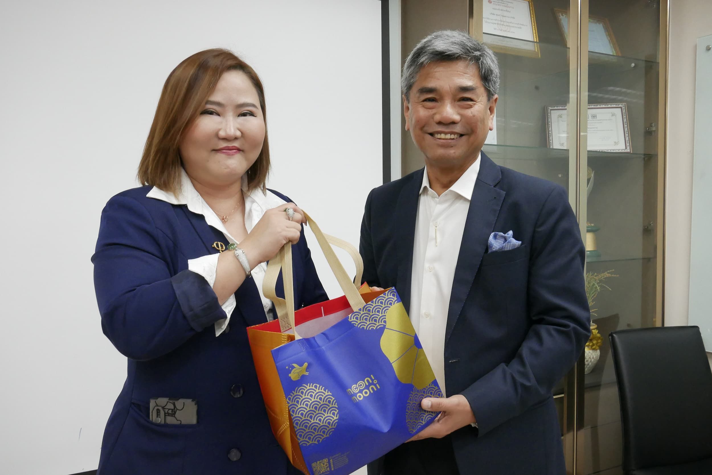 Two smiling individuals, a woman and a man, exchanging a colorful gift bag.