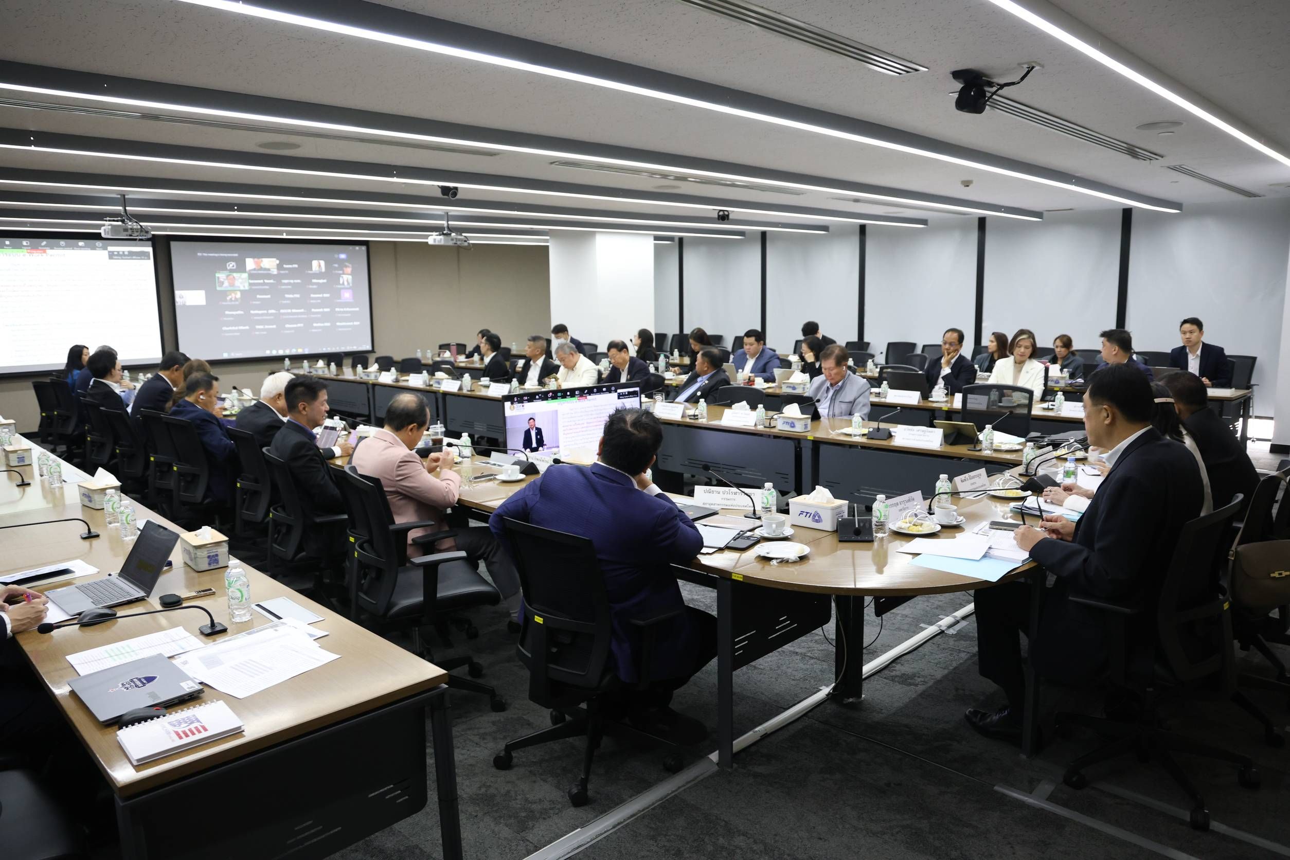 A group of professionals attends a meeting in a modern conference room with projection screens.