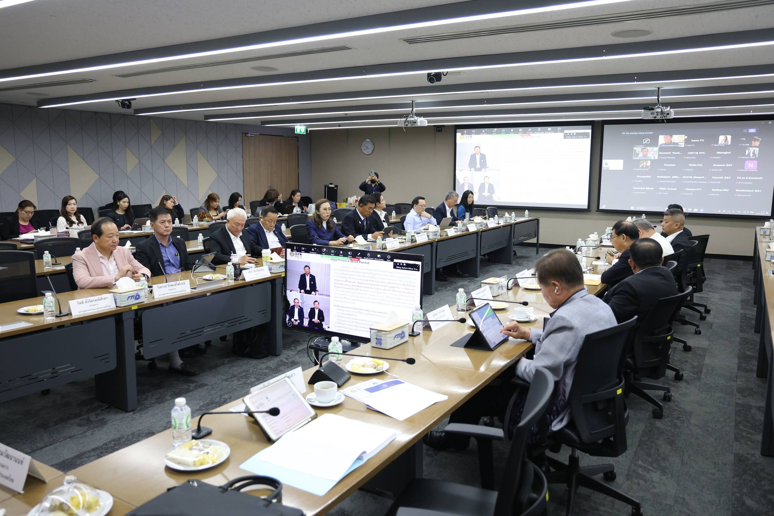 Professionals attend a hybrid conference in a modern meeting room with large screens.