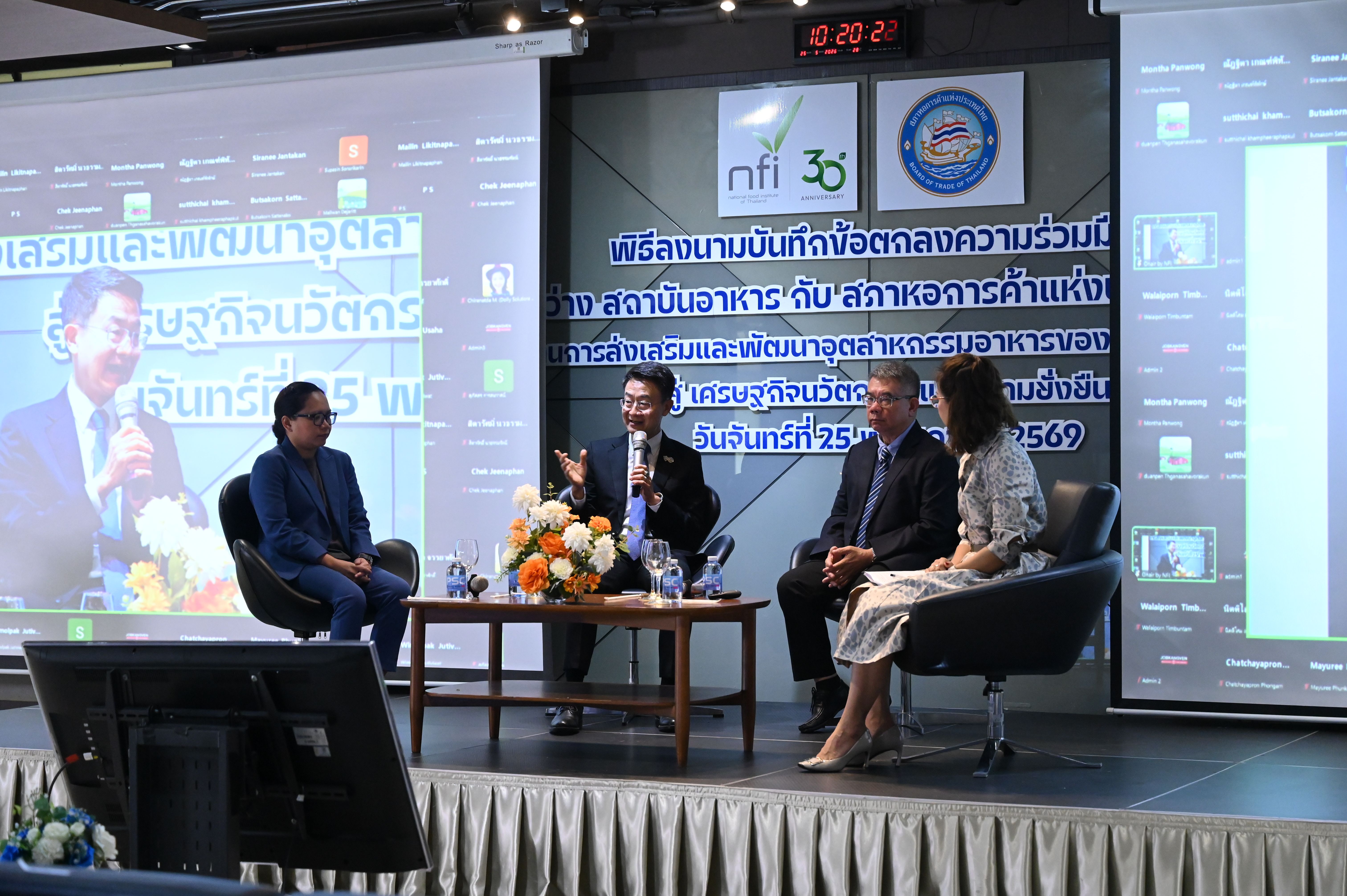 Four panelists engage in a discussion on stage, with one man speaking and gesturing.