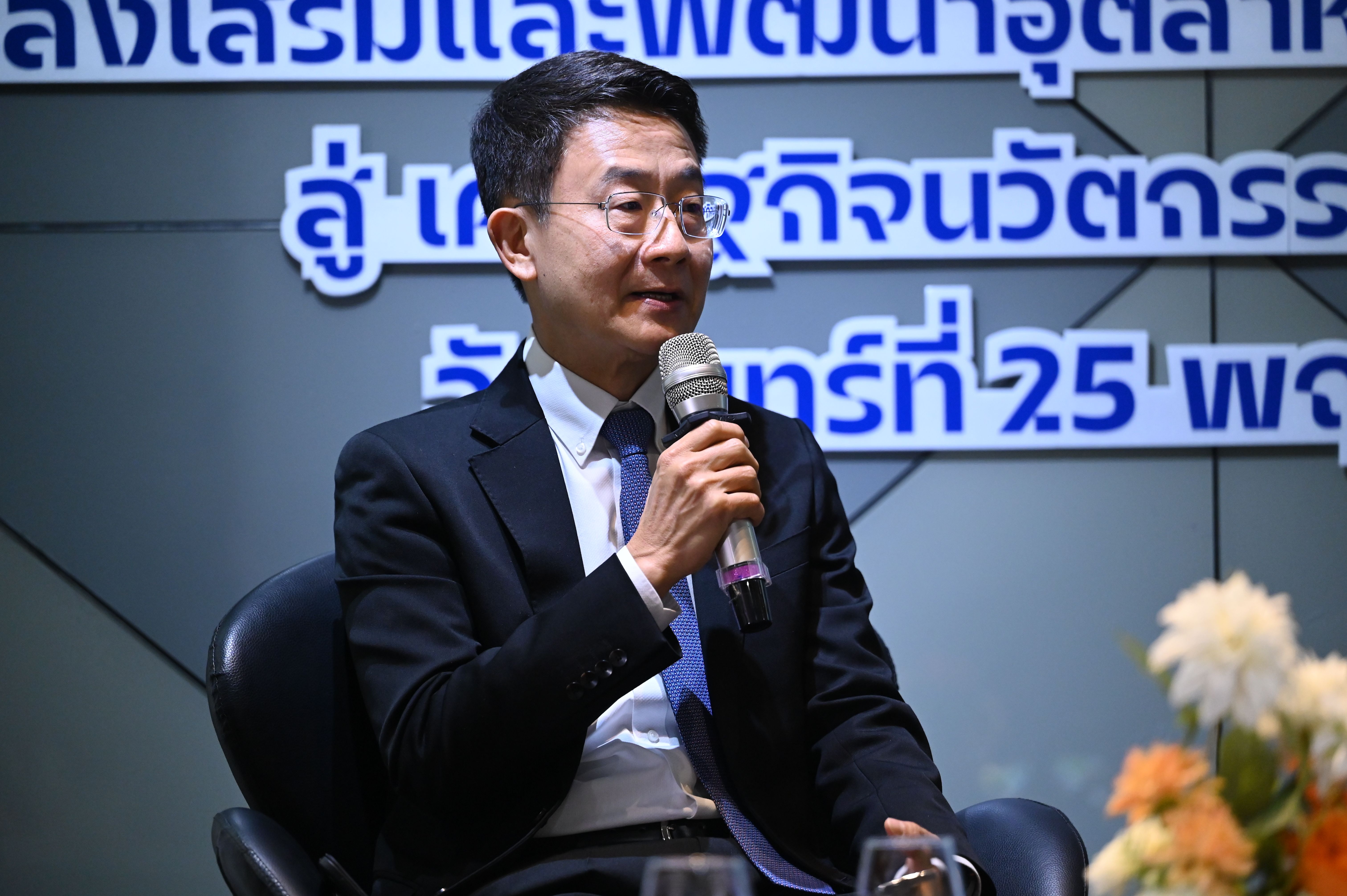 Man in glasses and a suit speaks into a microphone at a professional event.