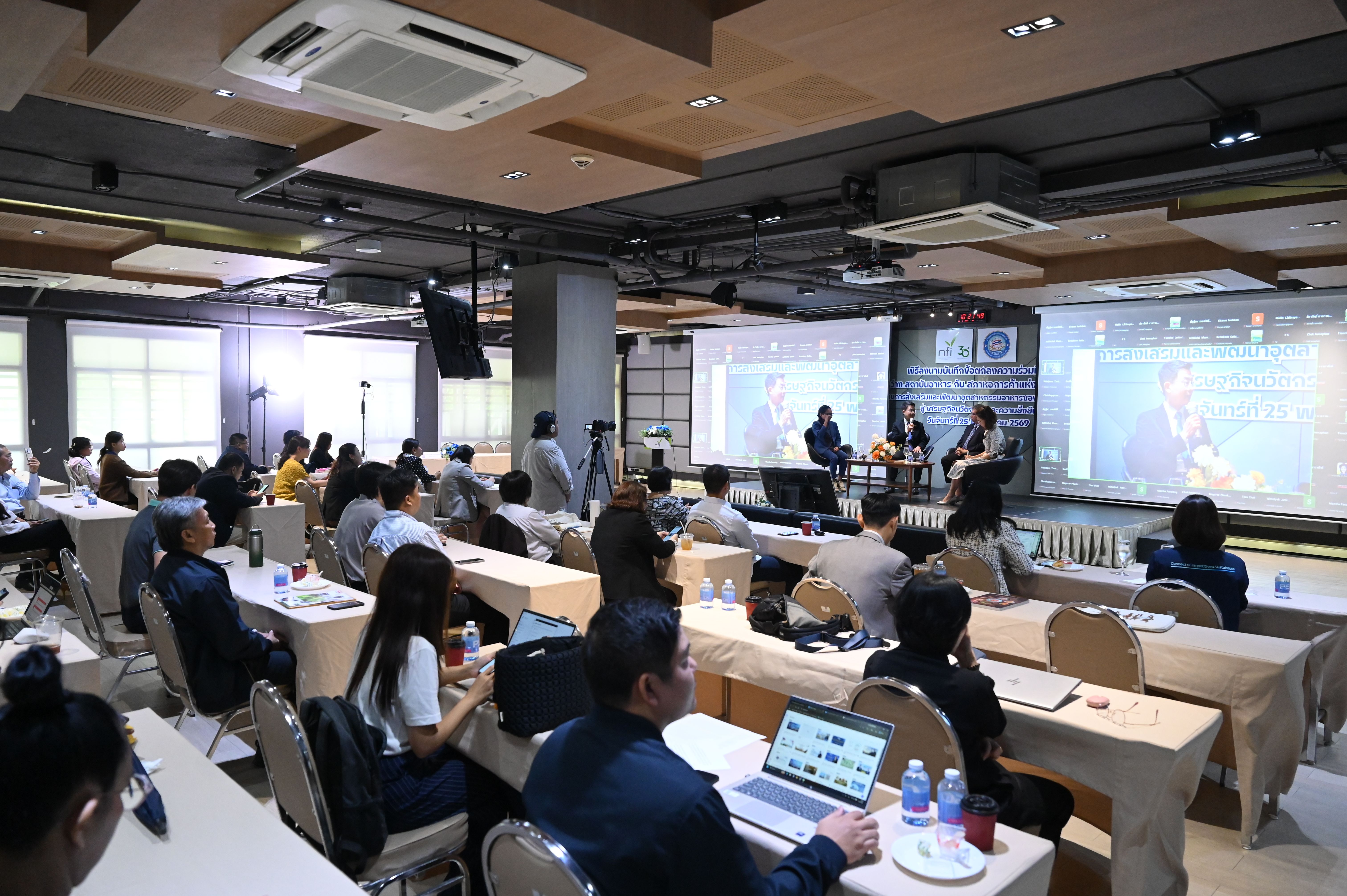 People gather in a conference room, attending a presentation with multiple screens.