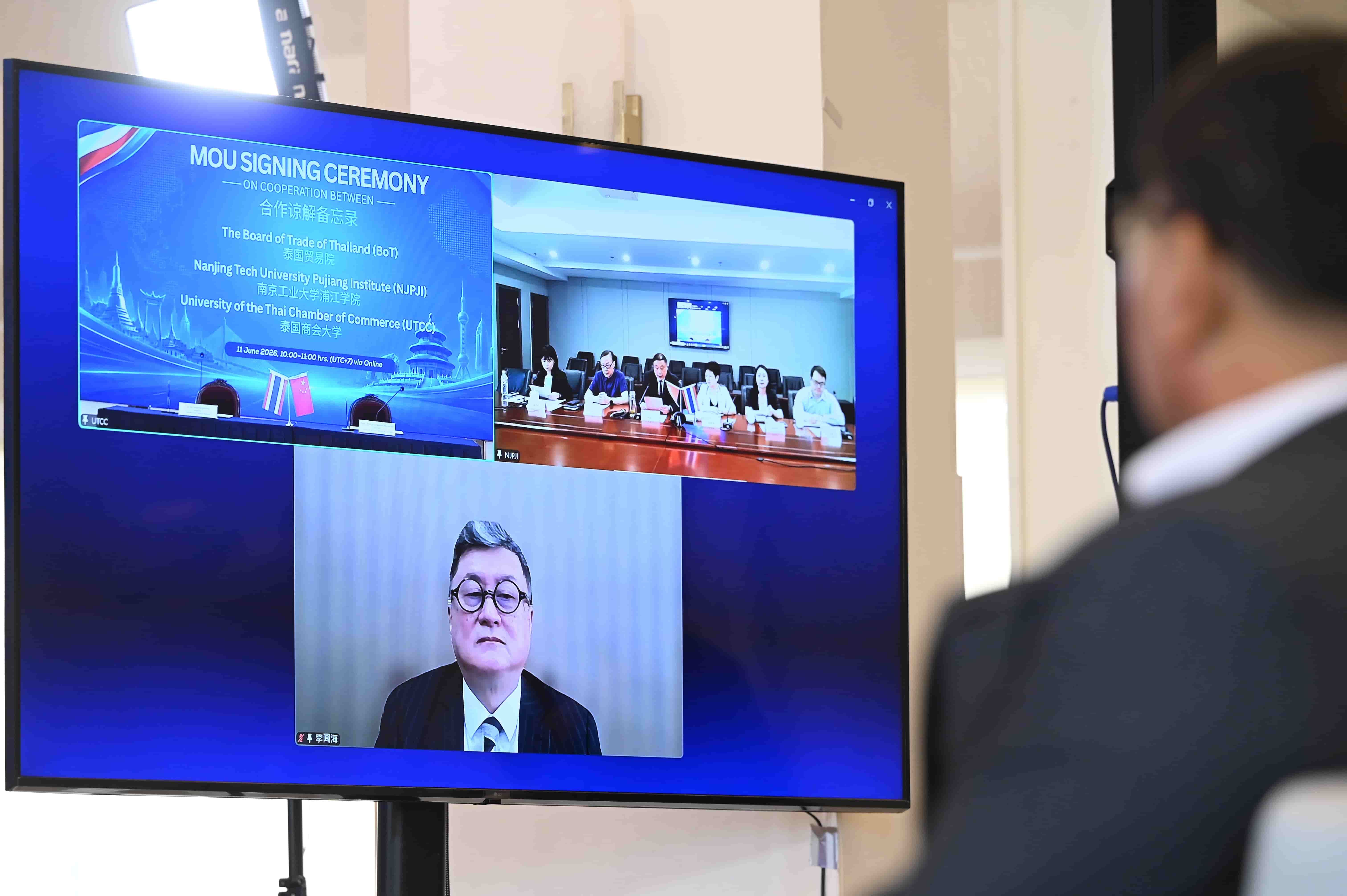 Man observes a virtual MOU signing ceremony displayed on a large screen.