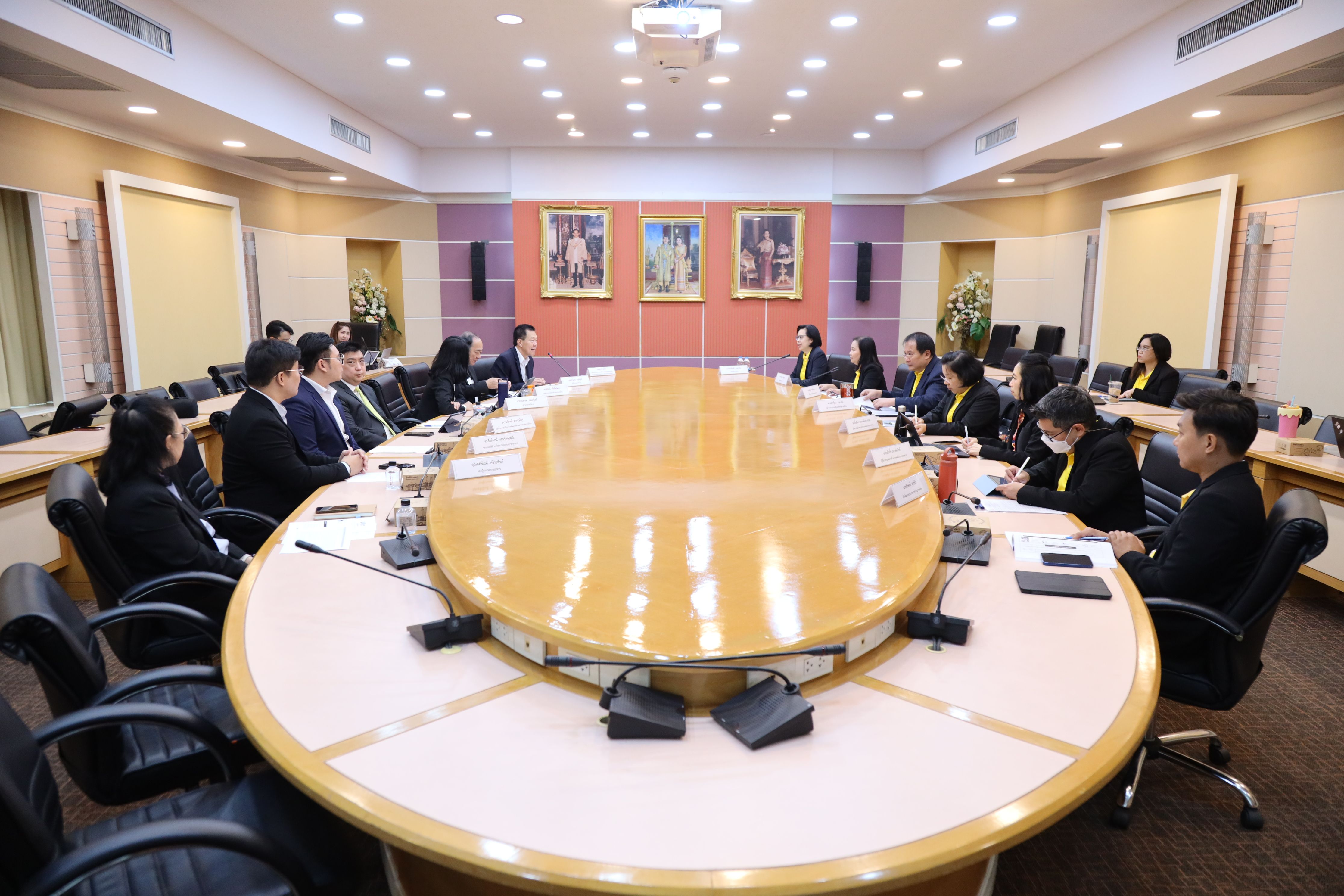 Professionals in suits attend a formal meeting around a large wooden conference table.