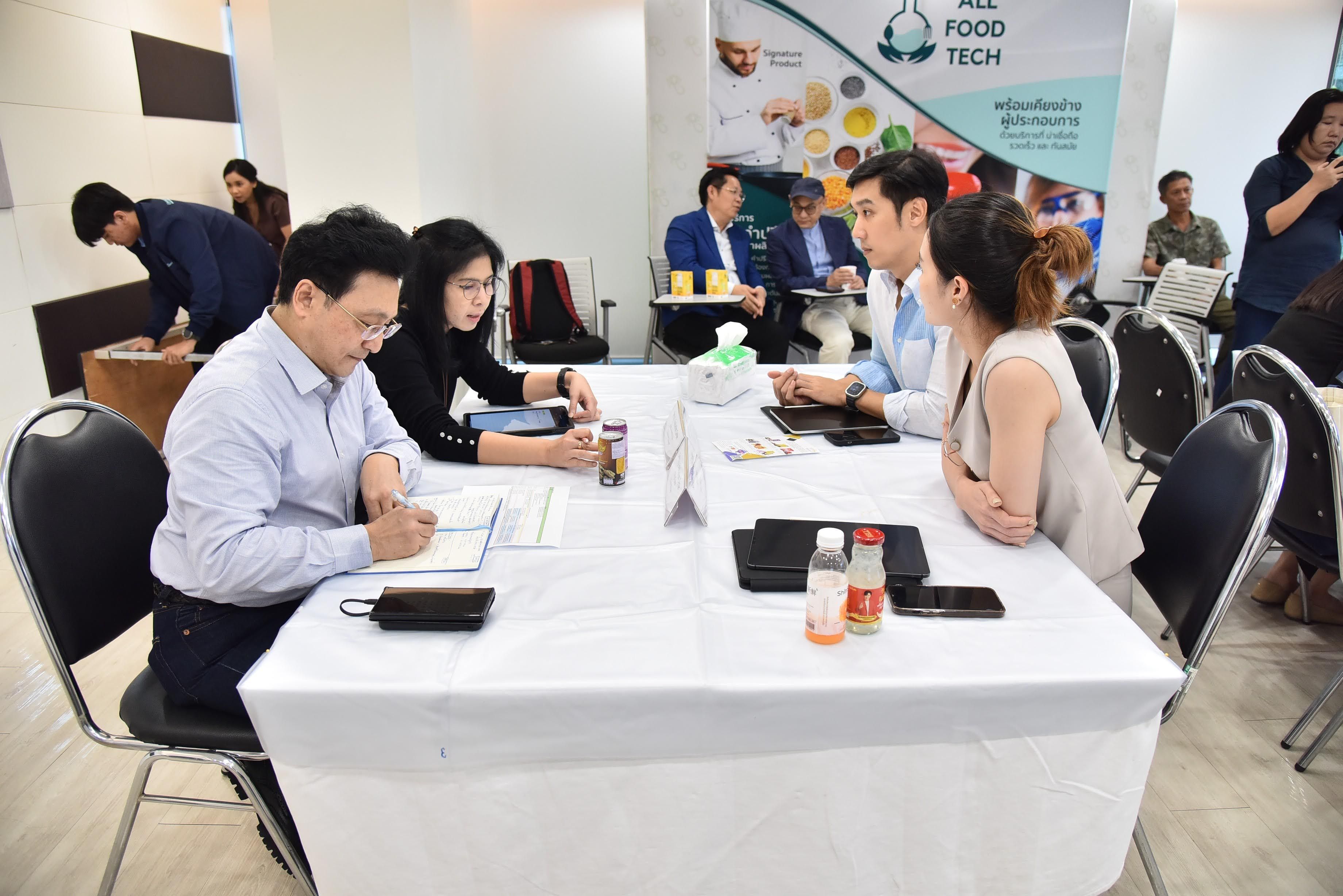 Four professionals are seated at a table, discussing and writing, at a food tech event.