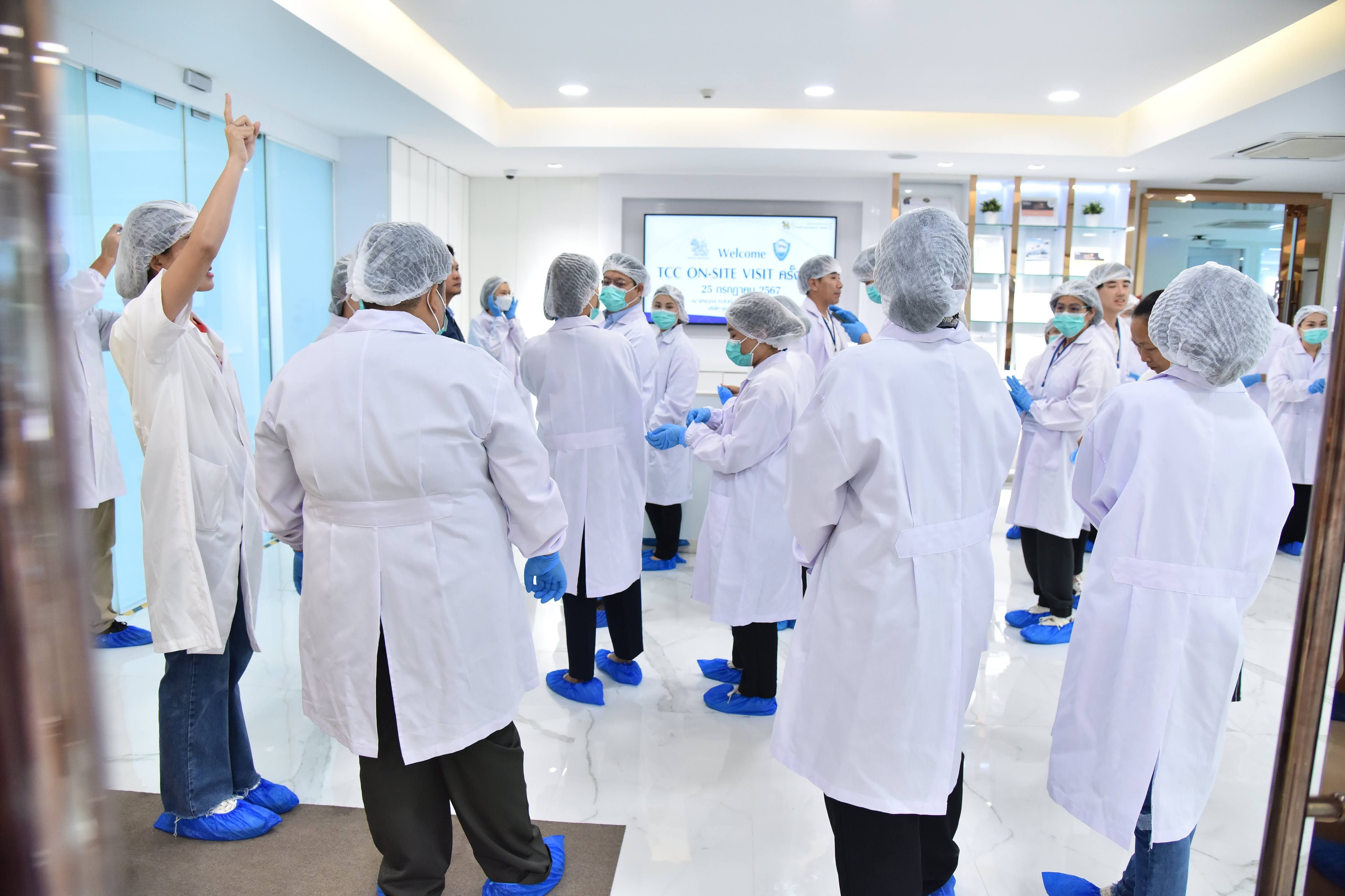 Group of people in lab coats, hairnets, and shoe covers in a sterile environment.