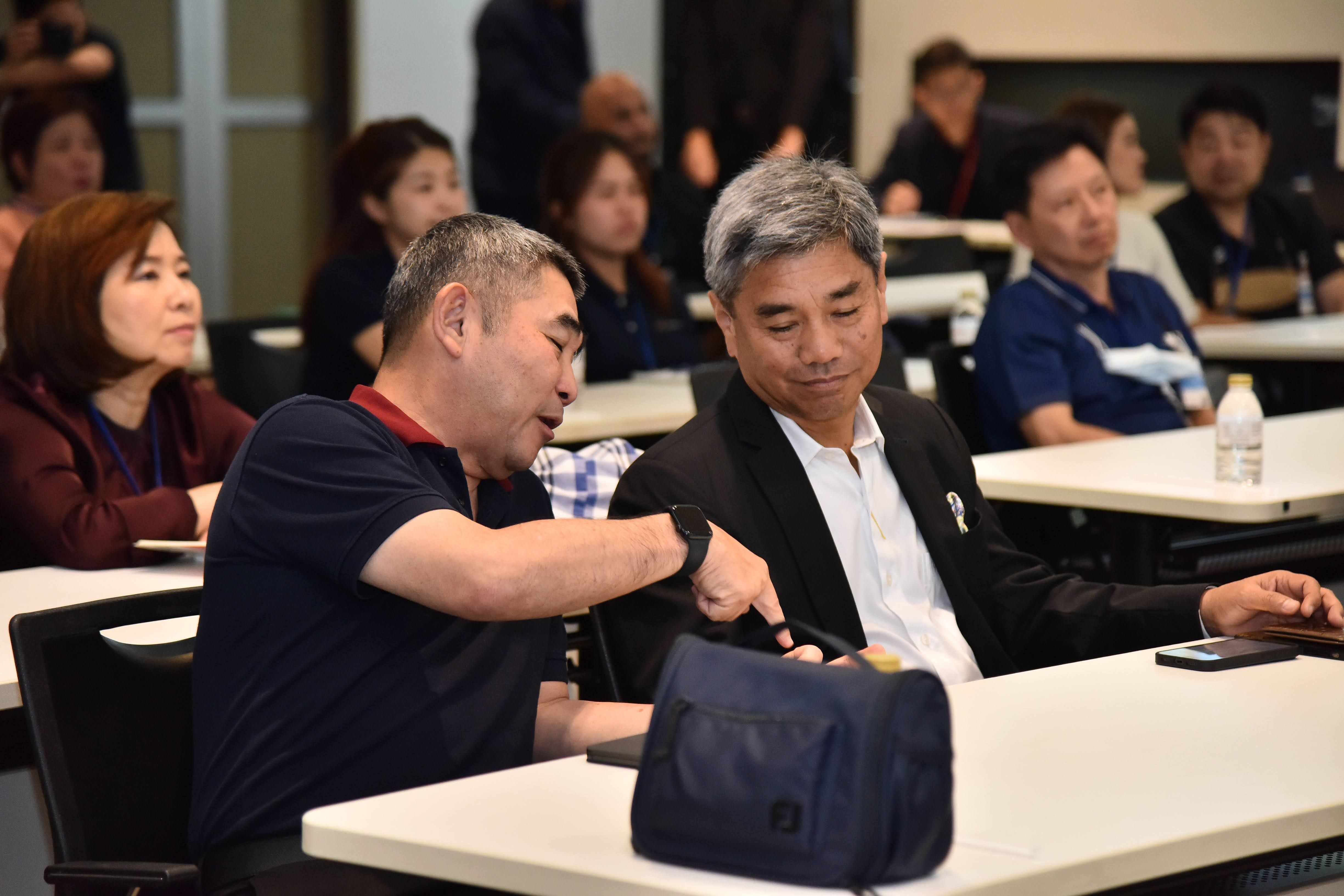 Two men in a conference room examine an item inside a dark bag.