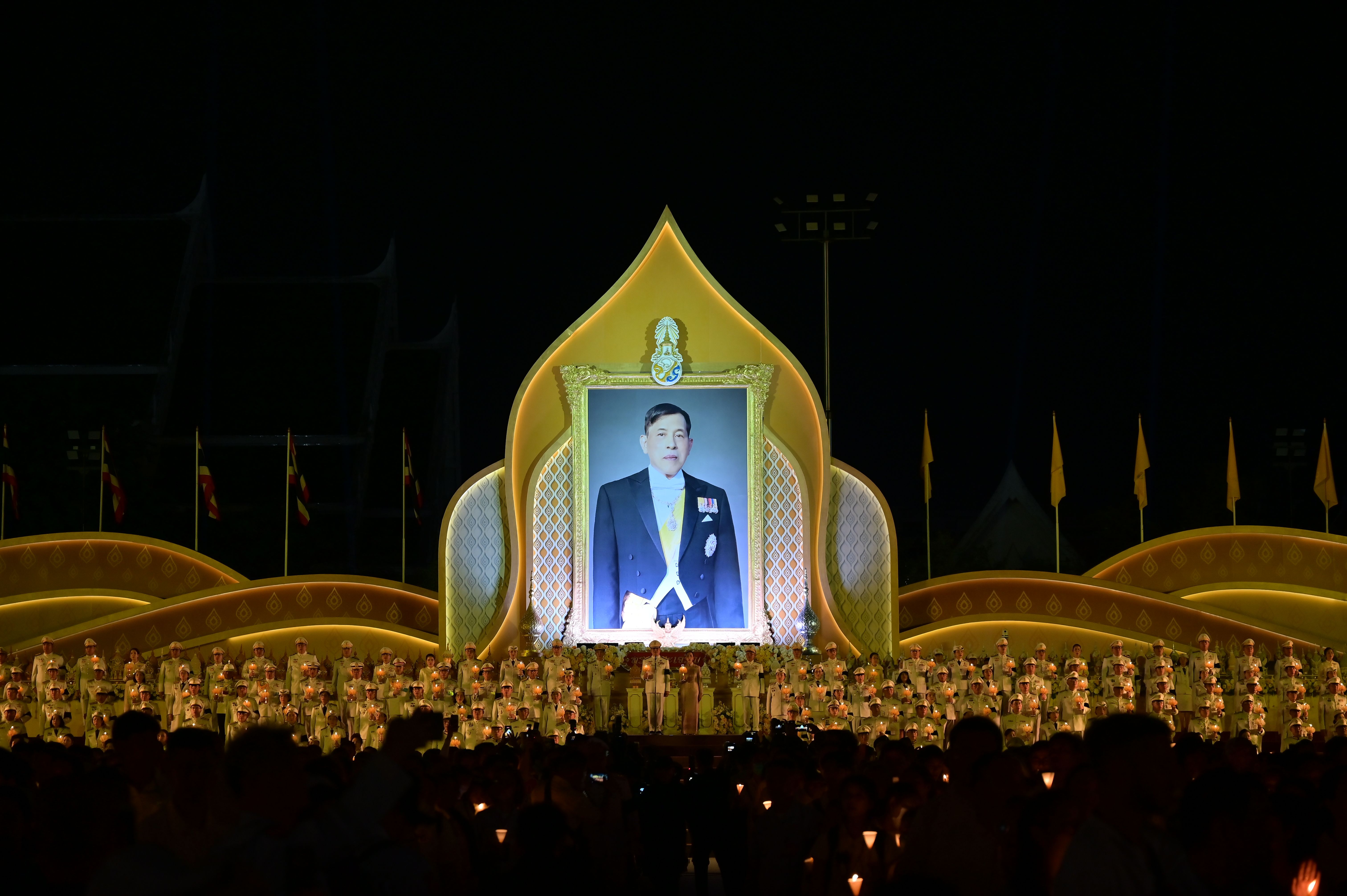 Large golden framed portrait of a king illuminated during an outdoor night ceremony.
