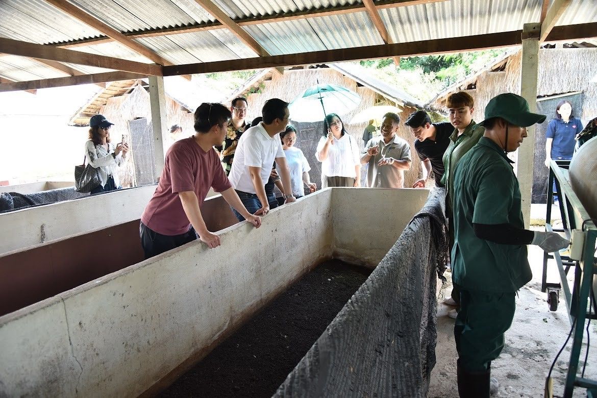 Visitors inspect long composting beds filled with organic material at an agricultural facility.