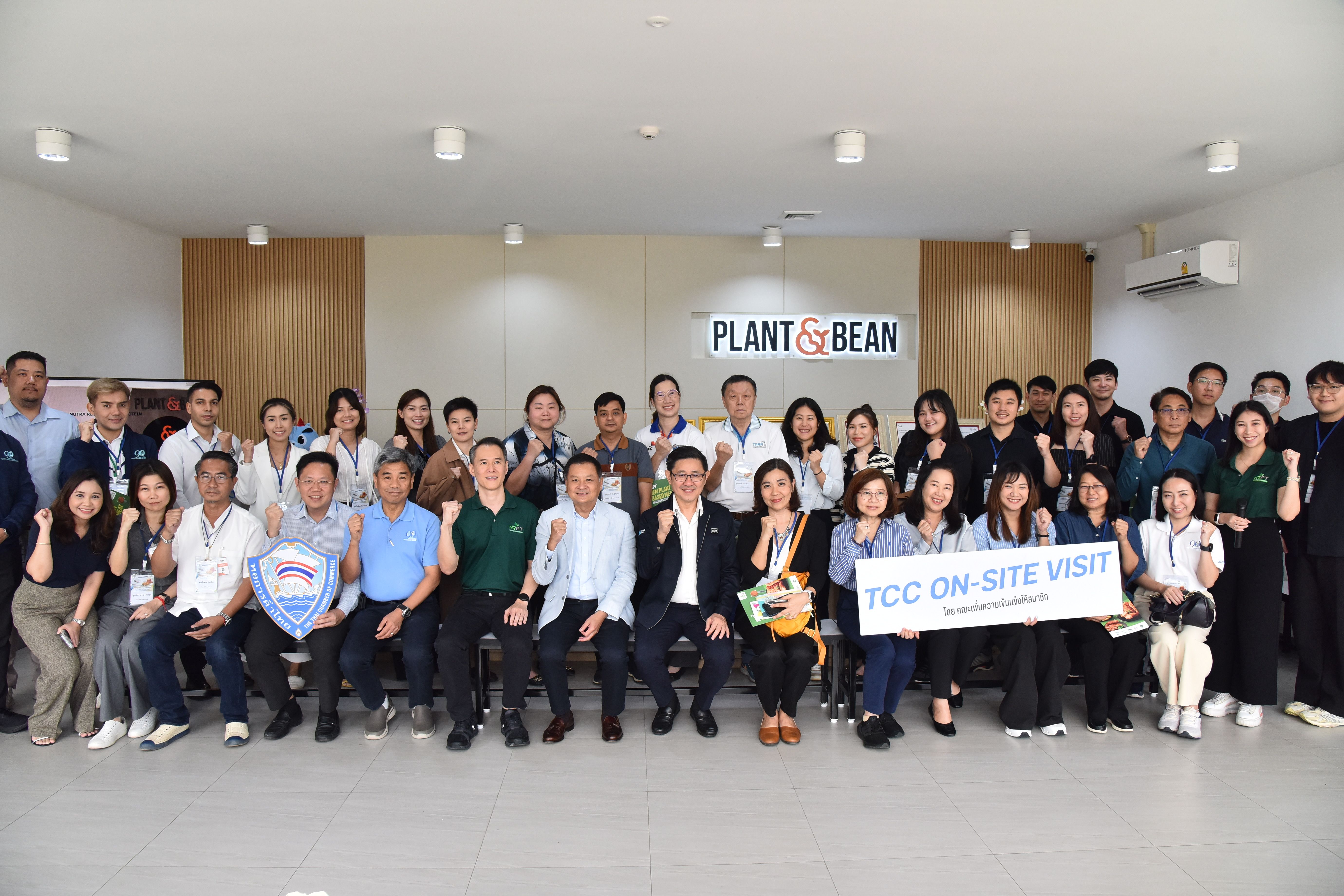 A large group of smiling professionals poses for a photo at a "PLANT & BEAN" facility.