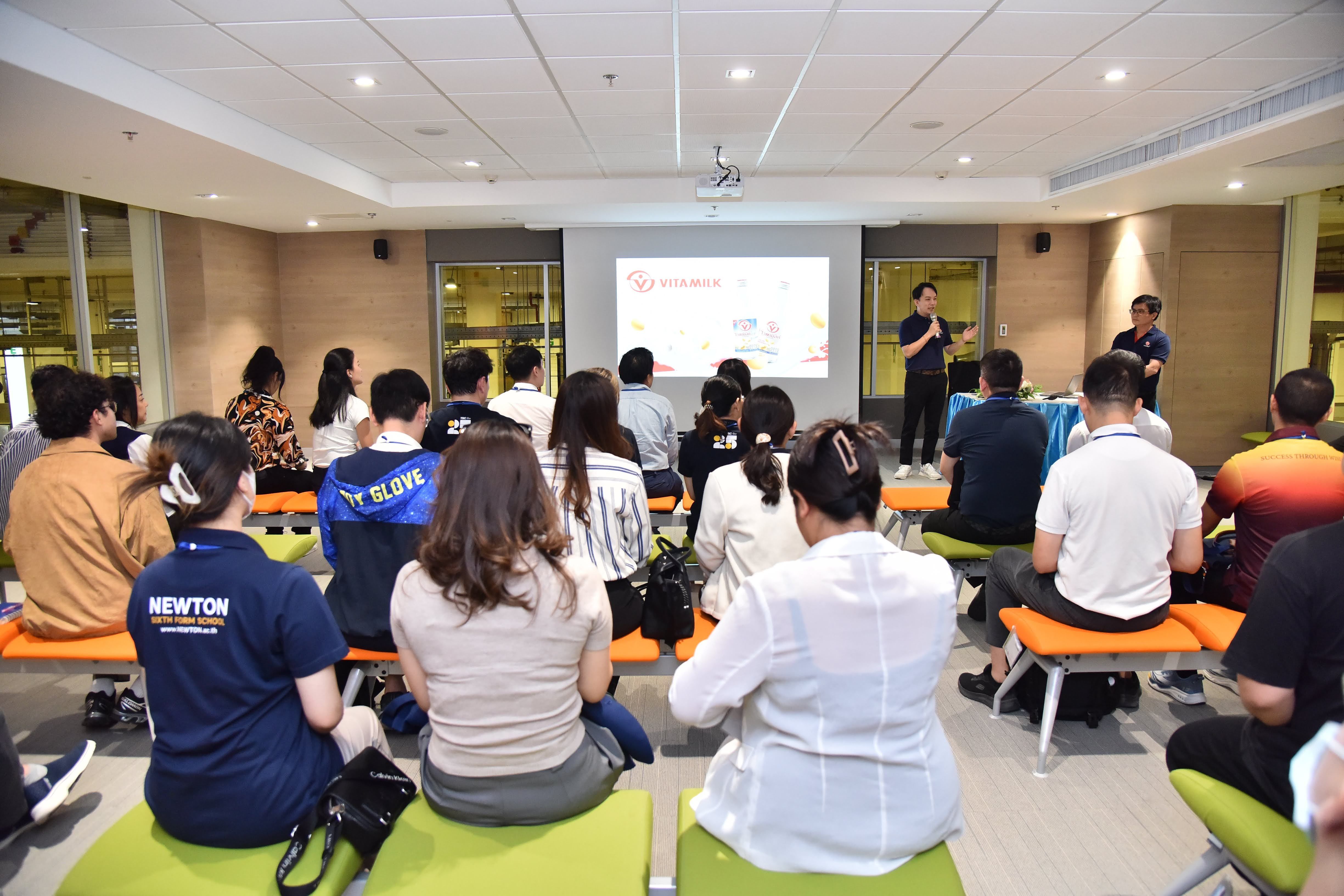 Attendees listen intently to two speakers presenting on a screen at an indoor seminar.