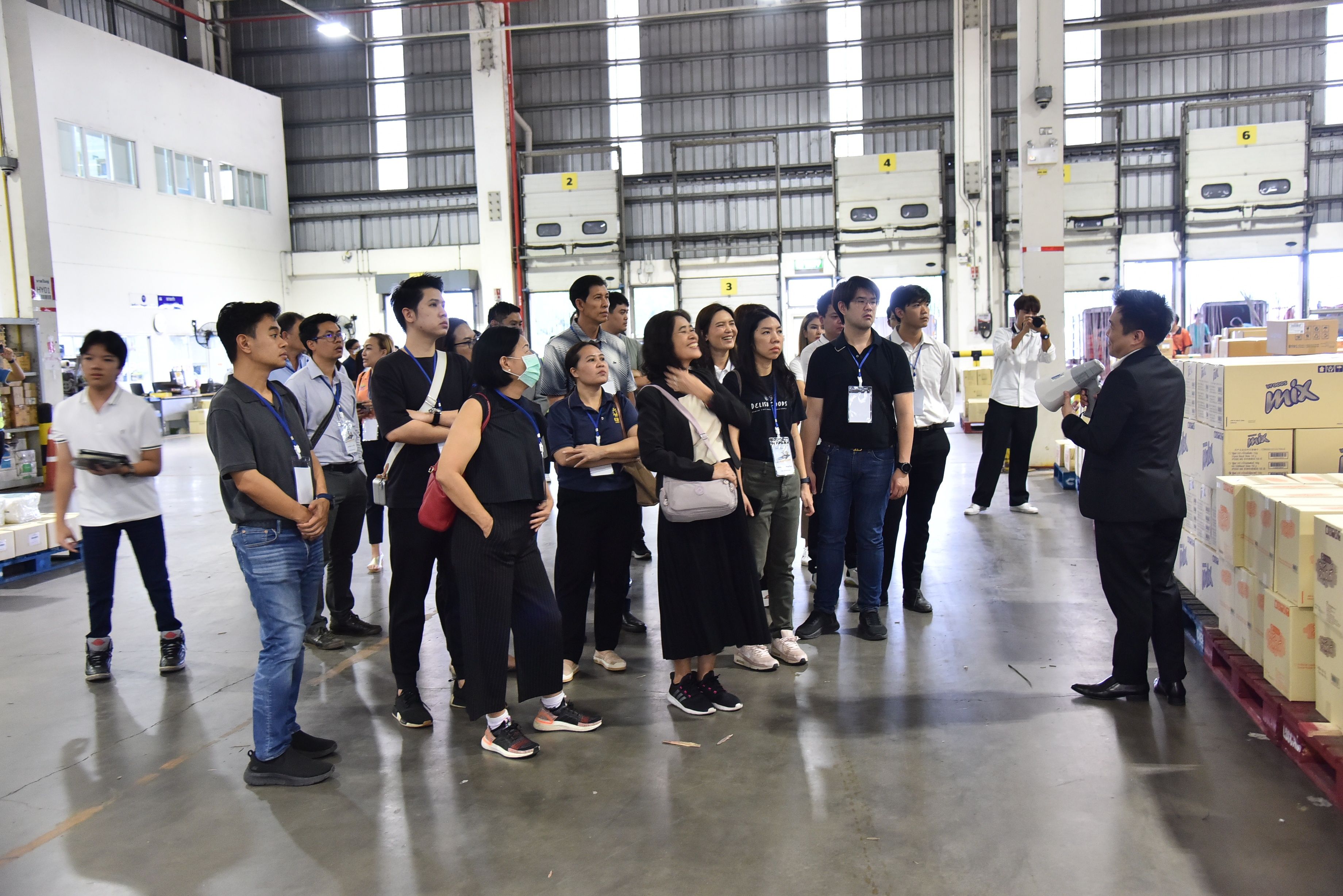 A diverse group listens attentively to a speaker in a modern warehouse setting.