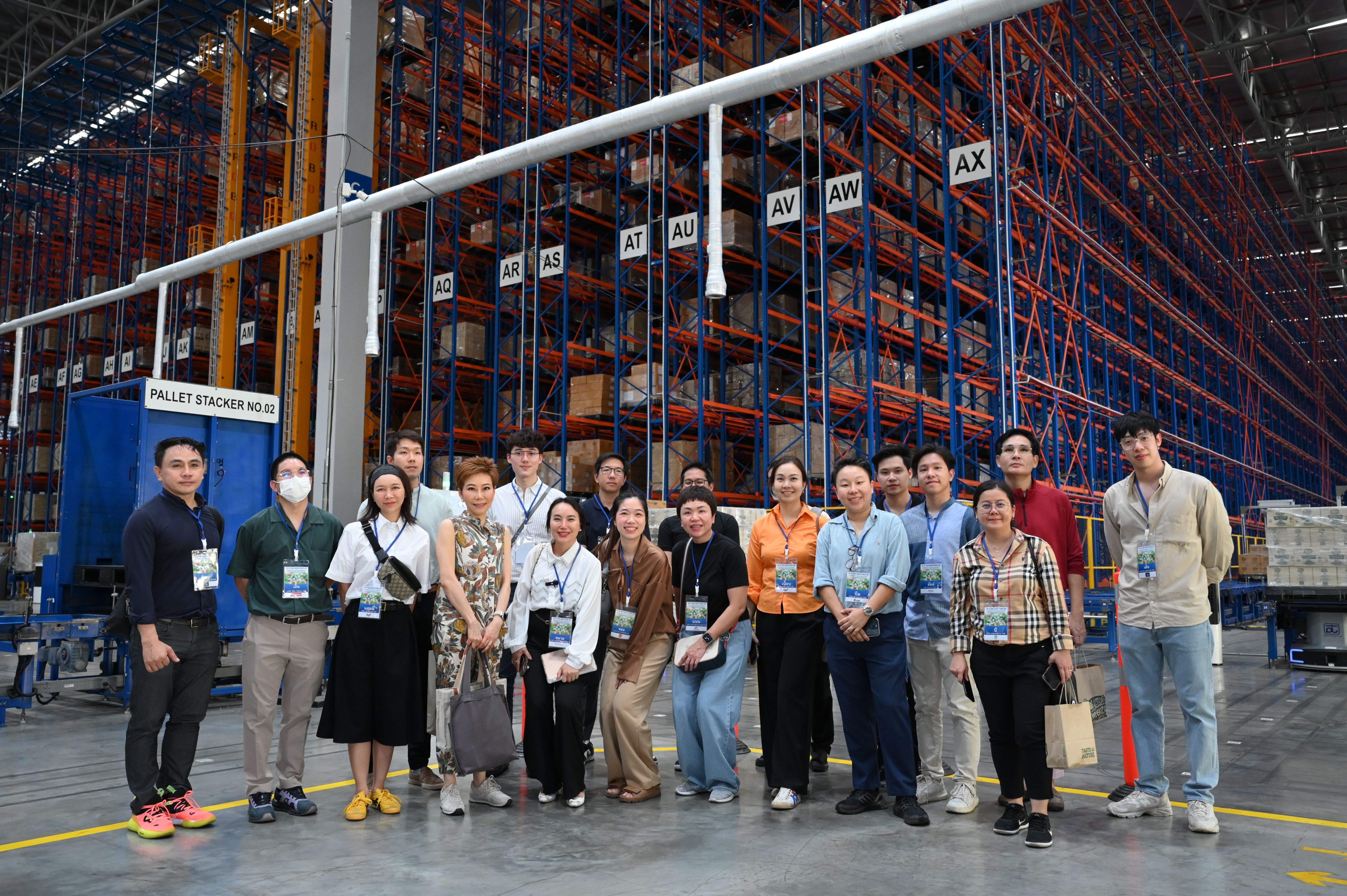 A group poses in a large warehouse with tall shelves stocked with various items.