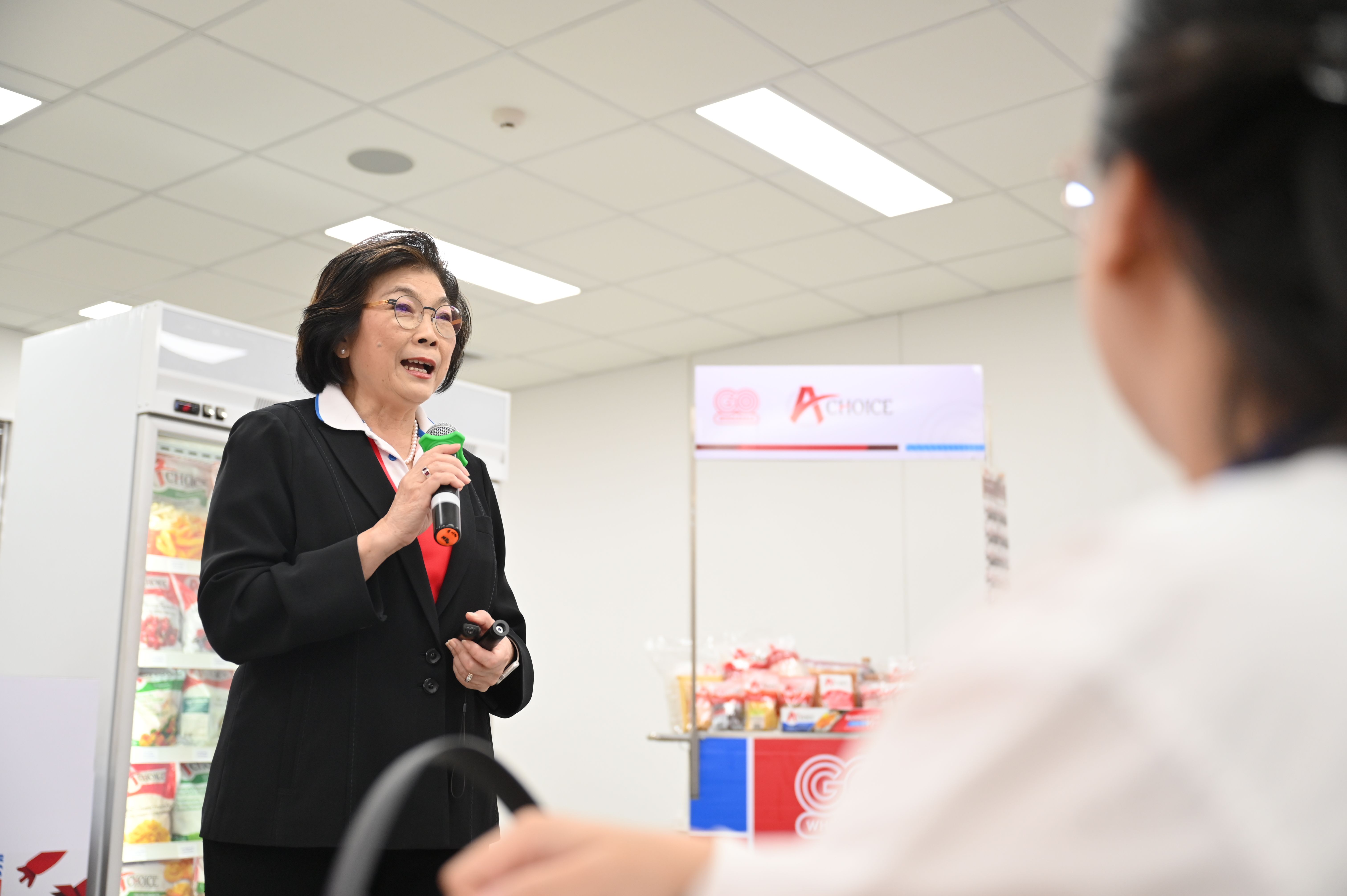 A professional woman speaks into a microphone at an A+ Mart promotional event.