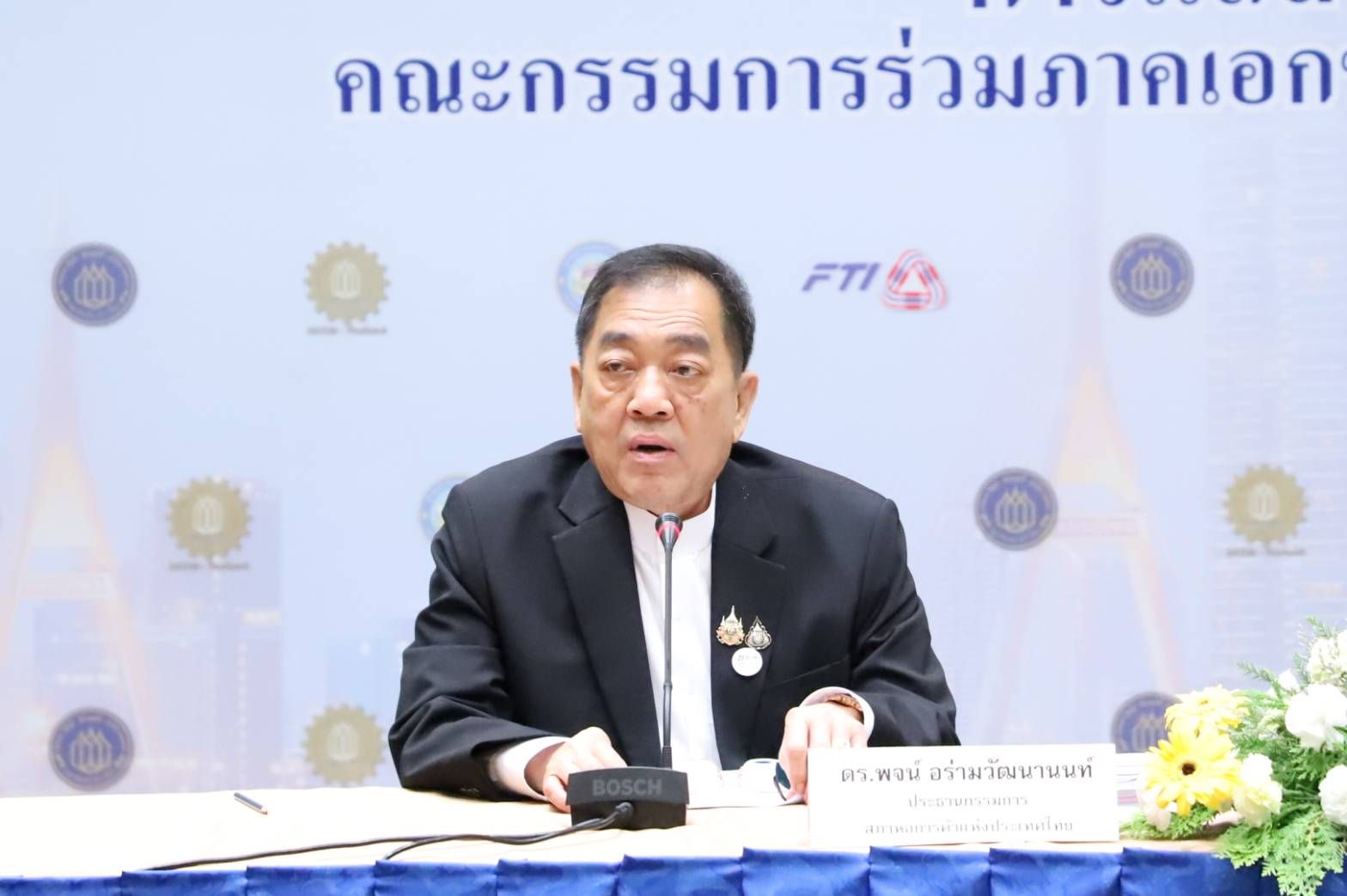 Man in black suit speaking at a podium with microphone during a formal event.