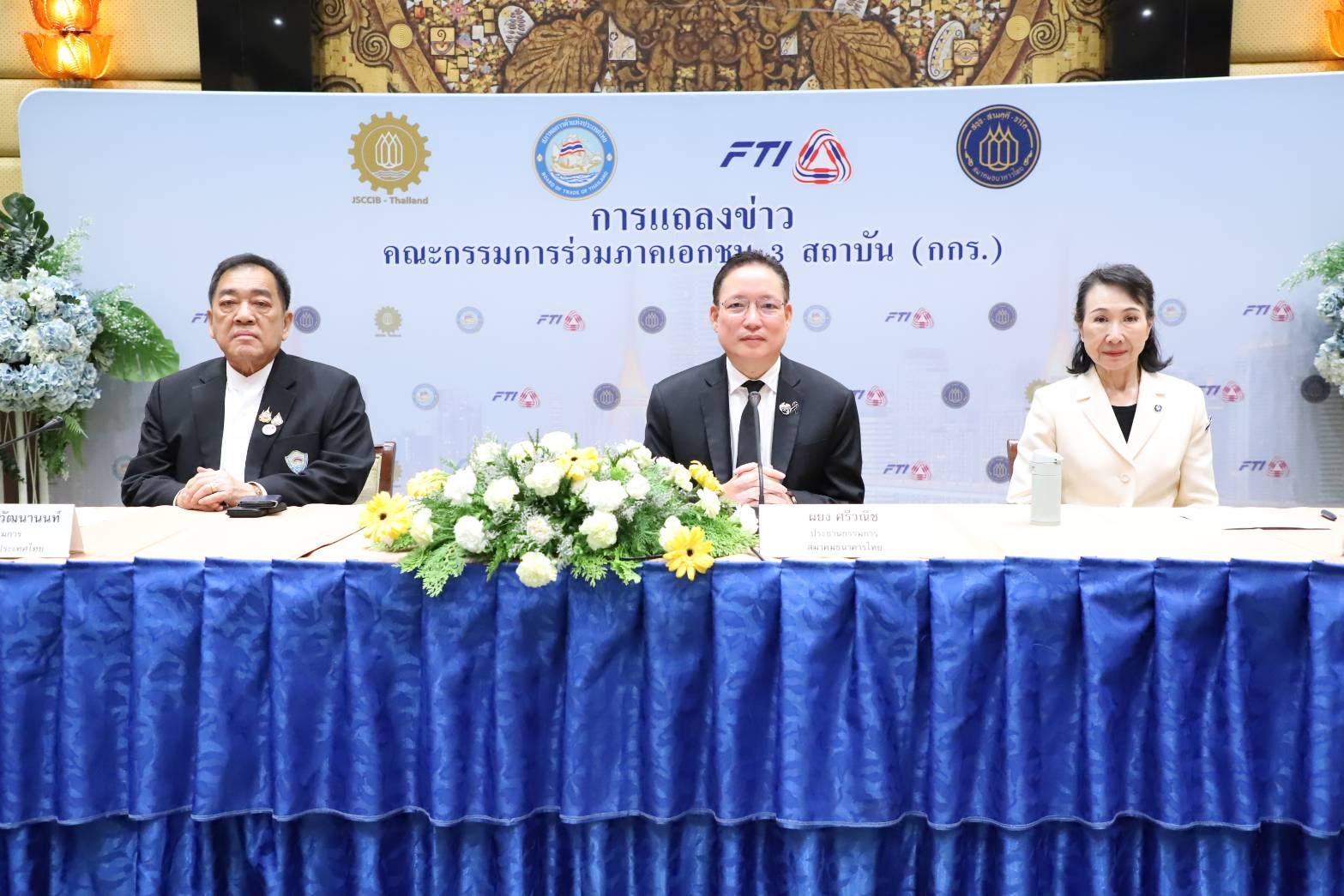 Three officials in formal attire sit at a blue table during a press conference.