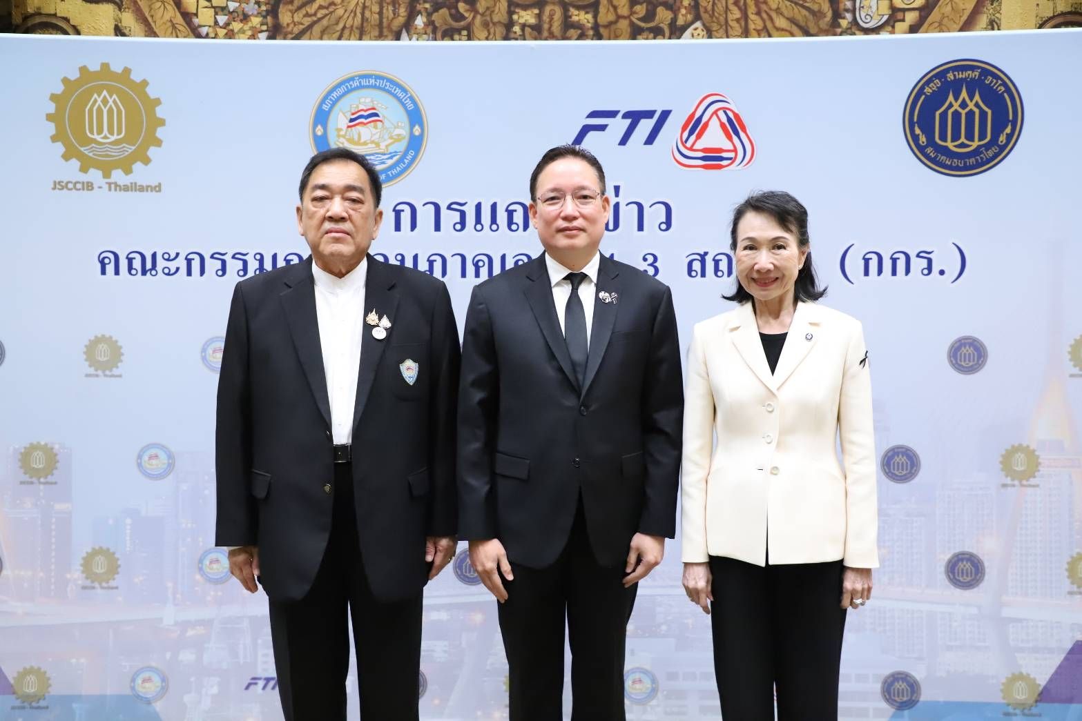 Three formally dressed executives, two men and one woman, stand before an FTI logo backdrop.