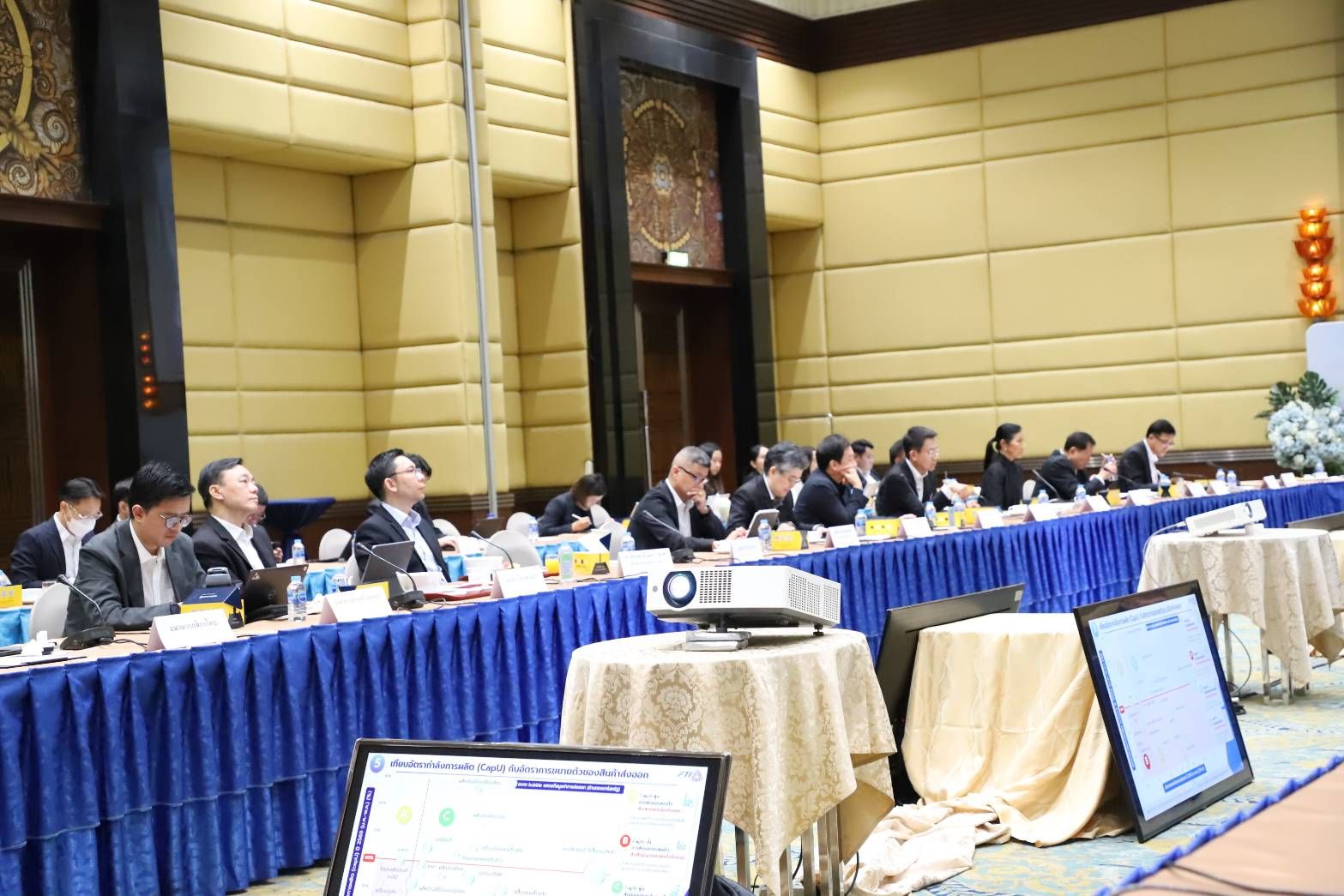 Professionals attend a conference, seated at long tables with a projector and laptop.