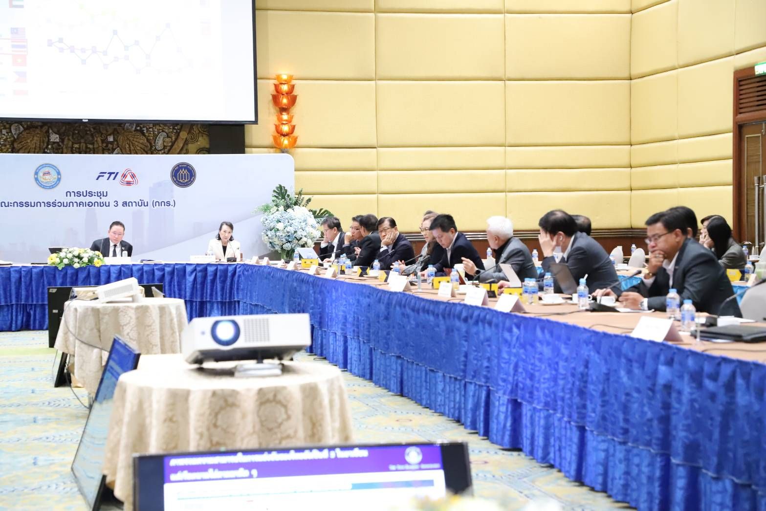 A professional conference with attendees seated at a long table, projector in foreground.