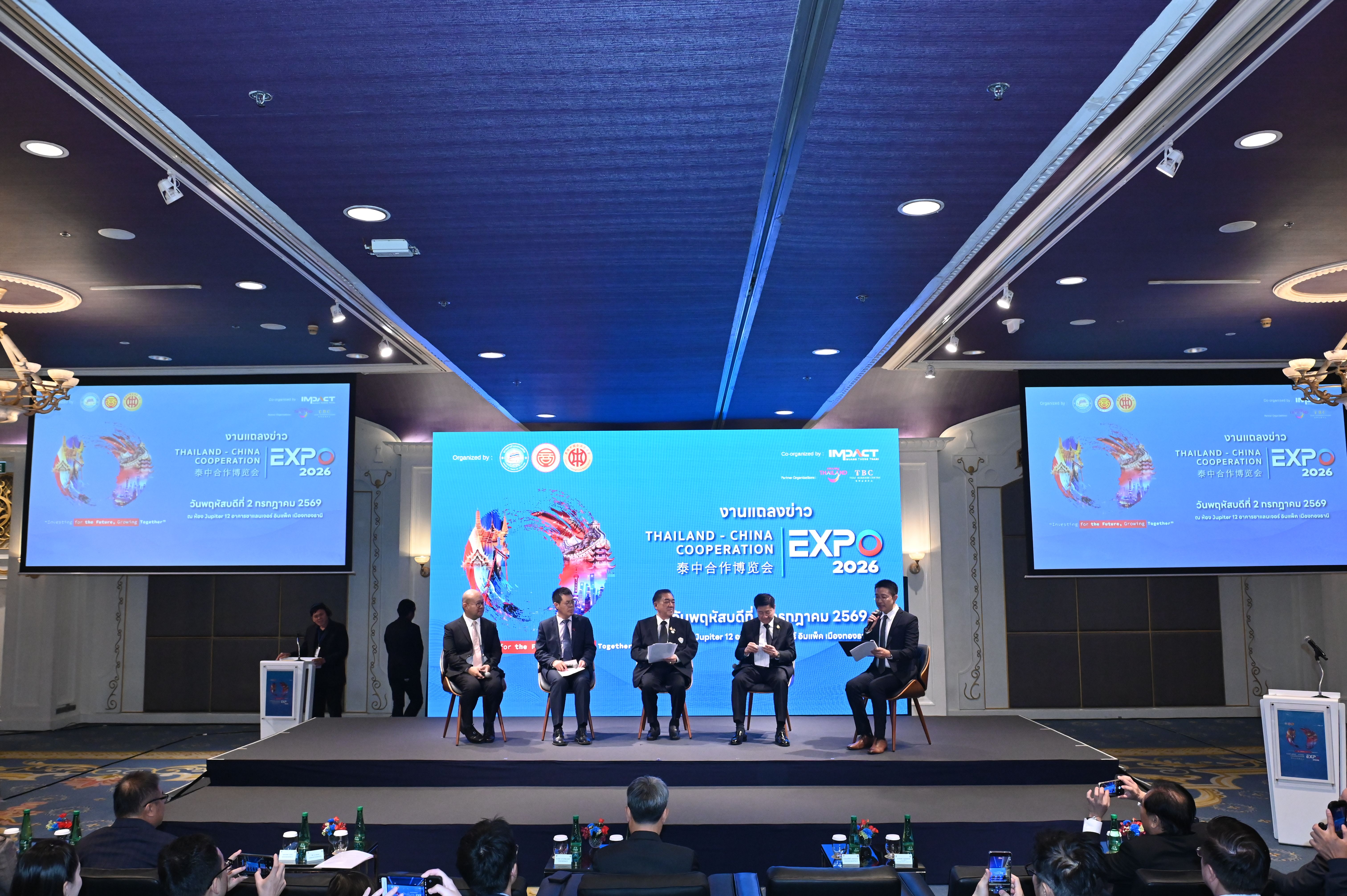 Panel discussion on stage at a conference with multiple speakers and large display screens.
