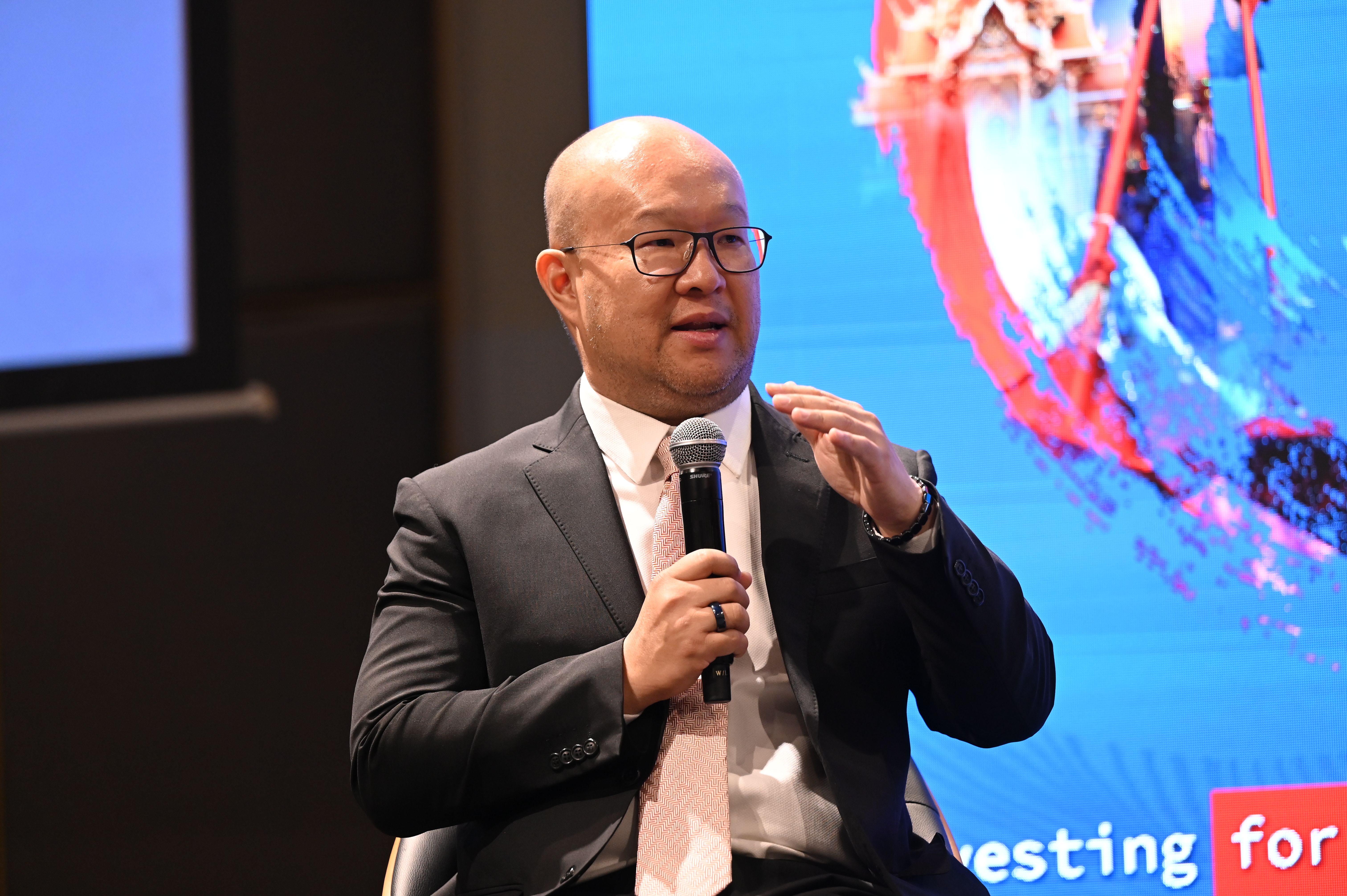 Bald man in glasses and dark suit speaks into a microphone during a presentation.