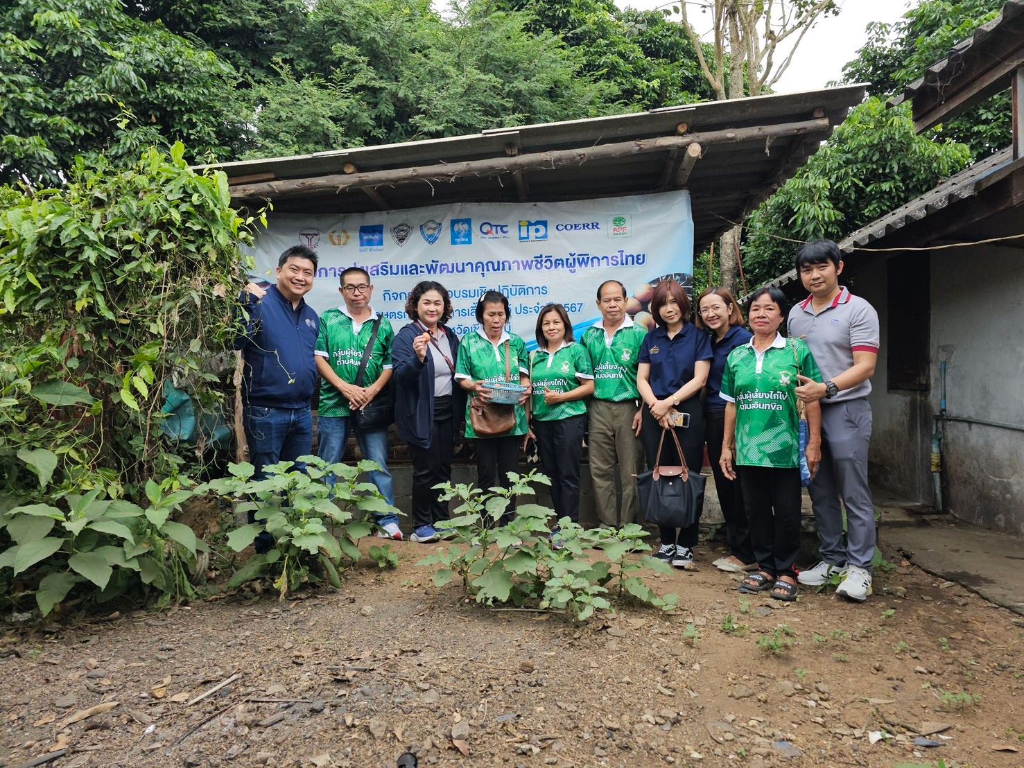 Group of people in green shirts stand before a banner and building in a natural setting.
