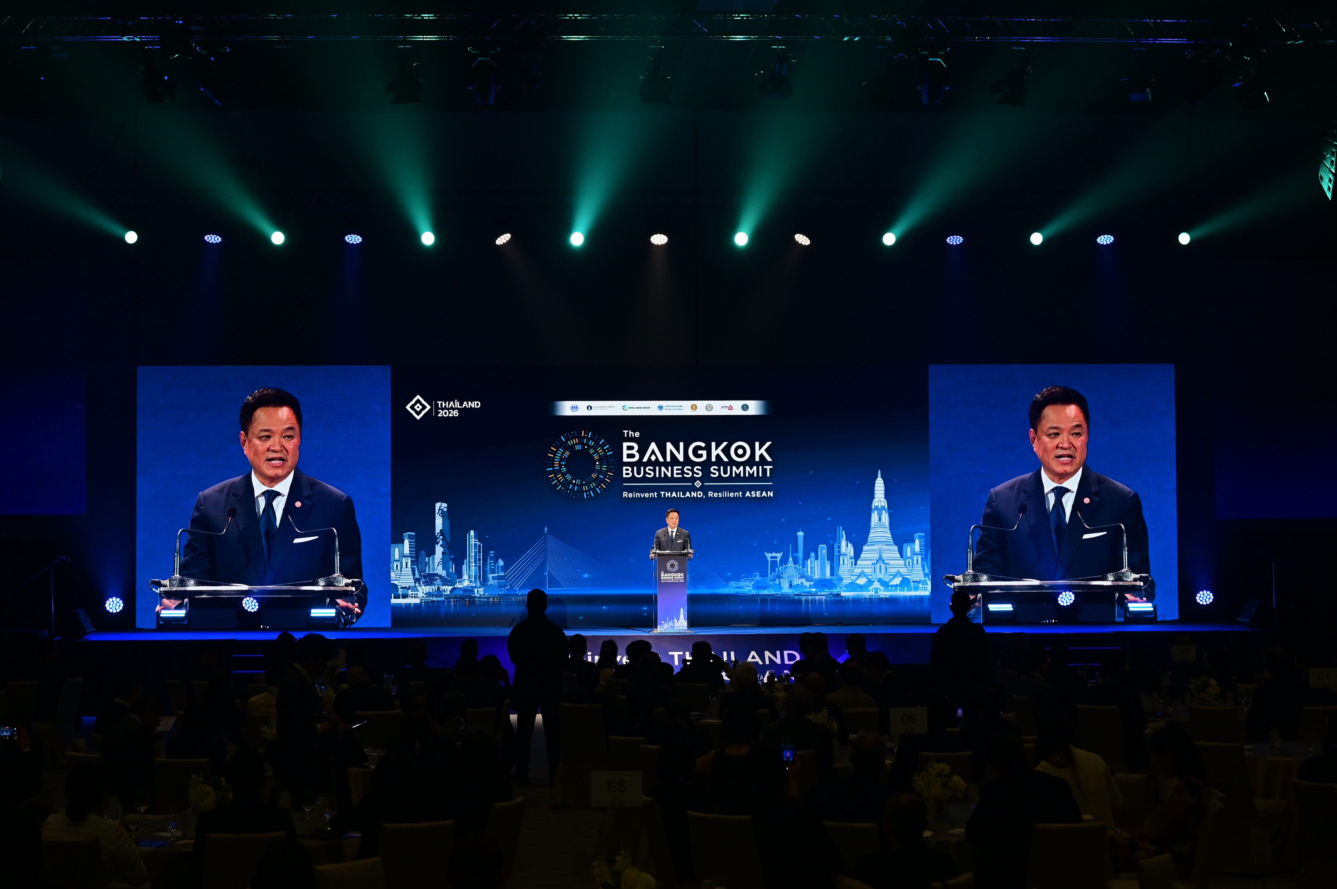 Speaker presents at The Bangkok Business Summit on a large stage with multiple screens.