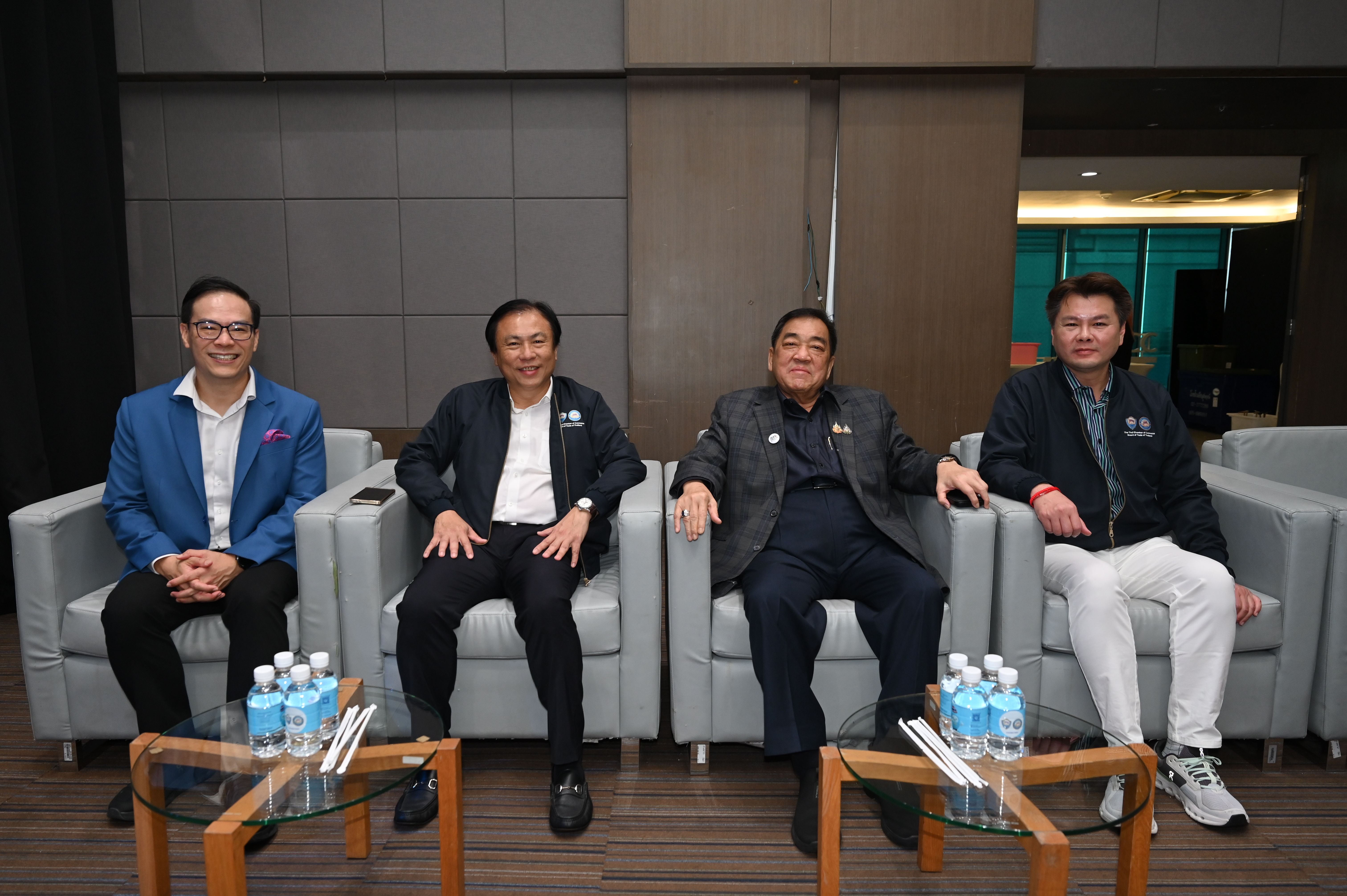 Four casually dressed men sit in modern chairs, posing for a photo indoors.