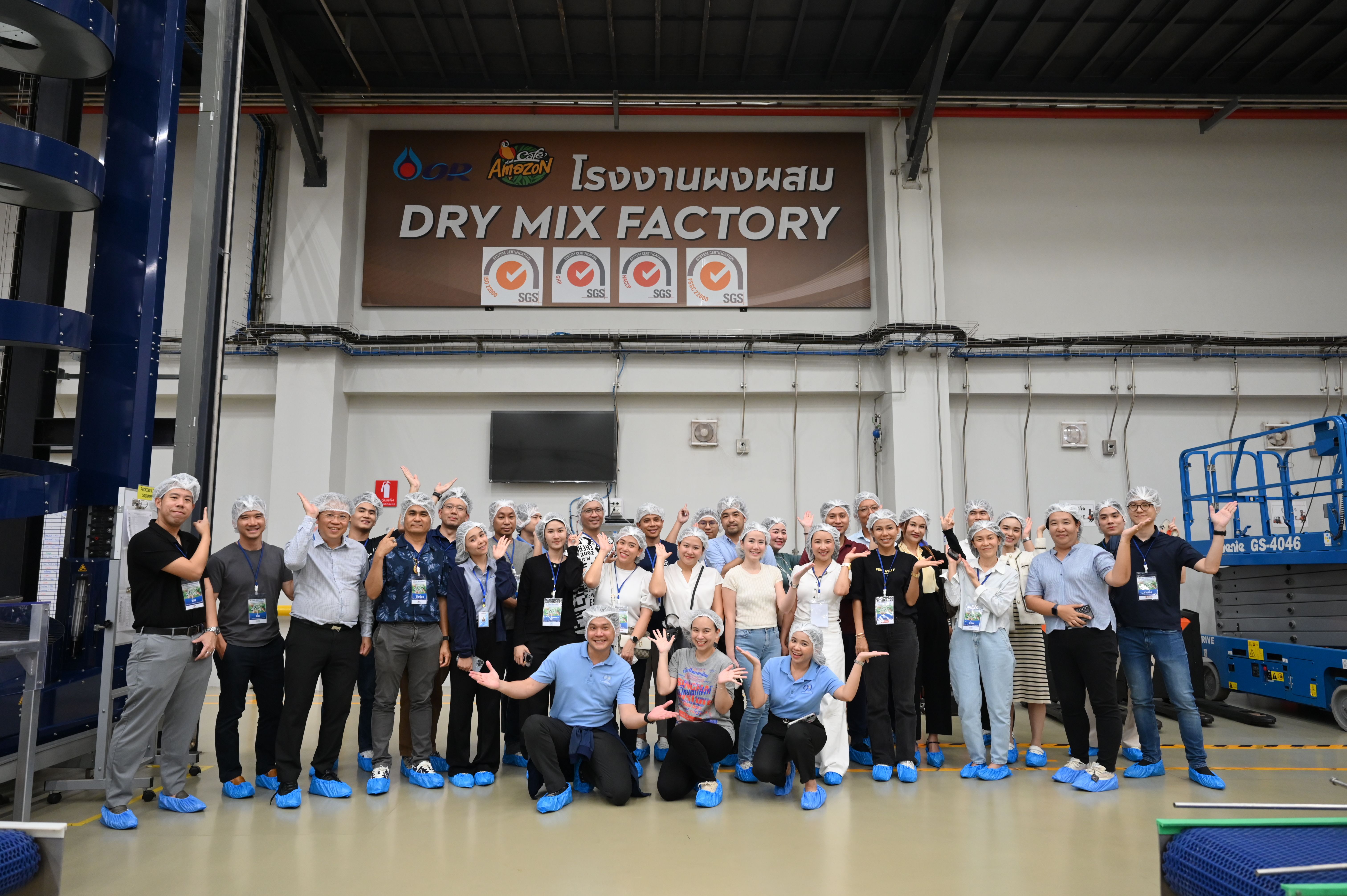 A large group of visitors poses for a photo inside a dry mix factory.